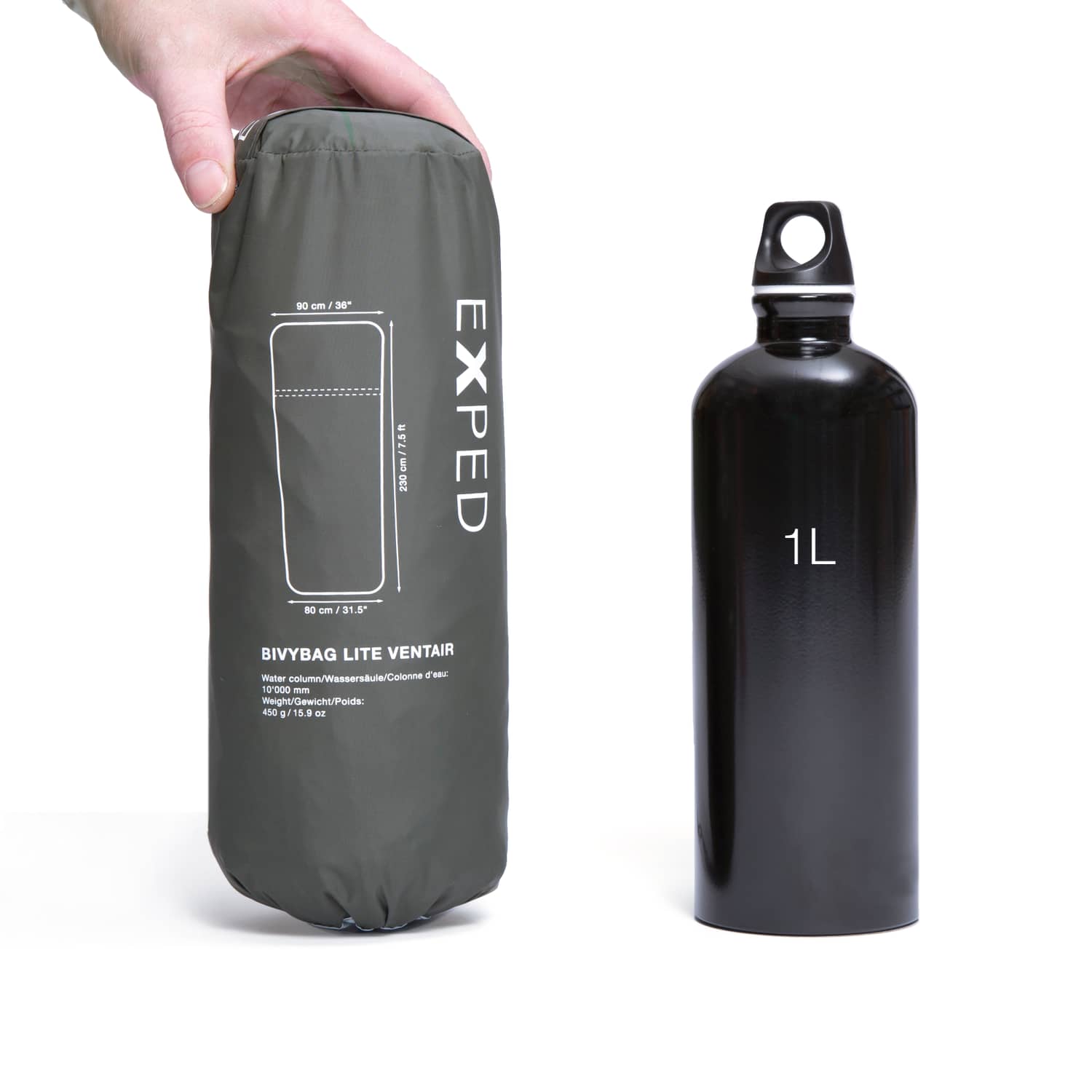 Eine Hand hält einen verpackten grünen EXPED Biwaksack Bivybag Lite Ventair/PU neben einer schwarzen 1-Liter-Flasche, beide aufrecht vor einem weißen Hintergrund zum Größenvergleich.