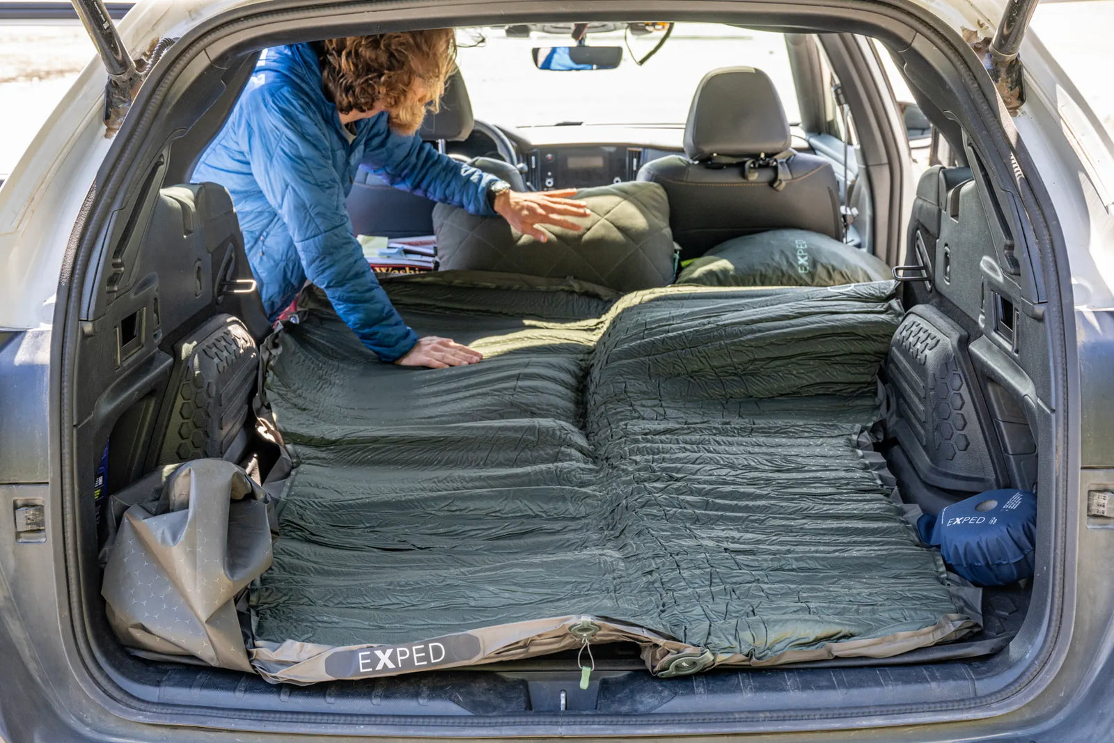 Die grüne EXPED Schlafmatte MegaMat Auto wird bei umgeklappten Rücksitzen in den Kofferraum eines Geländewagens gelegt, so dass eine flache, bequeme Schlafstelle für das Autocamping entsteht.