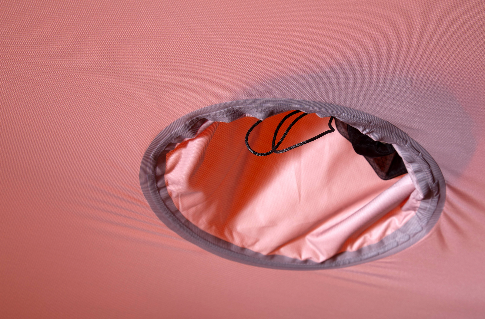 Eine Nahaufnahme einer kreisförmigen Öffnung aus rosa Stoff mit grauem Rand auf dem EXPED Zelt Polaris von EXPED, mit einem schwarzen Kordelzug im Inneren. Der strapazierfähige Stoff ist an den Rändern dieses Expeditionszeltes leicht gedehnt.
