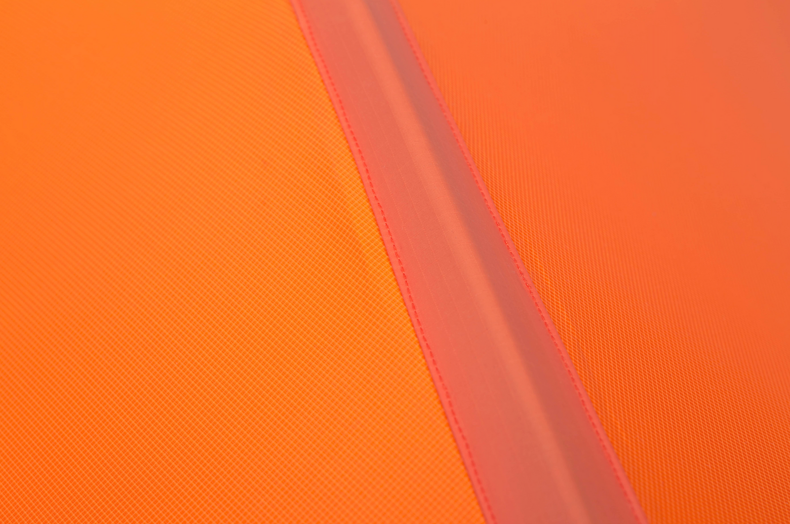 Nahaufnahme einer strukturierten orangefarbenen Oberfläche mit einem diagonalen, matten Streifen und sichtbaren Nähten, die an die robusten, langlebigen Designelemente des EXPED Exped Zelt Polaris erinnern.