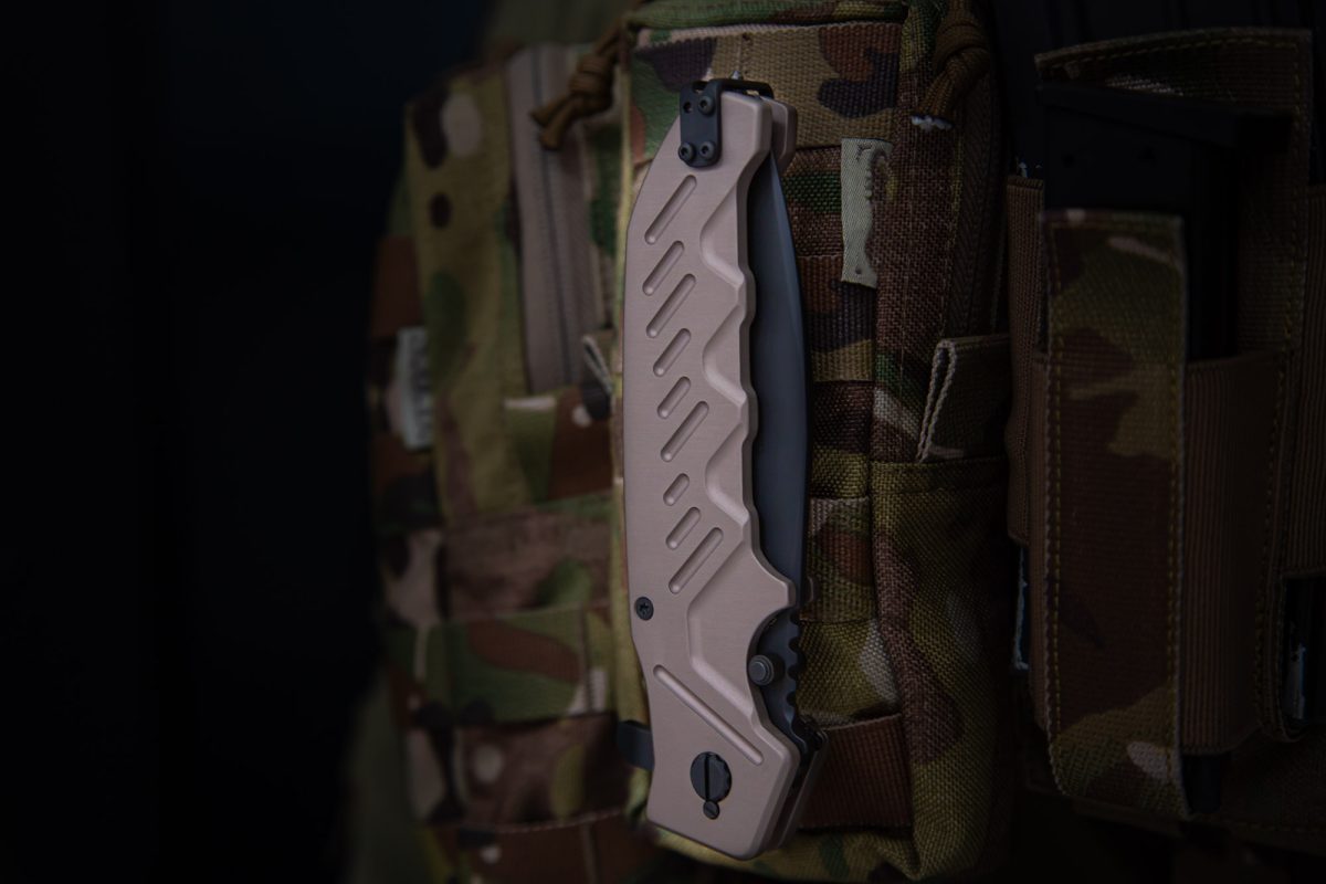 Ein hellbraunes Extrema Ratio Messer Glauca G1 von EXTREMA RATIO aus Böhler N690-Stahl wird auf der Vorderseite einer getarnten Militärweste mit mehreren Ausrüstungsfächern befestigt.