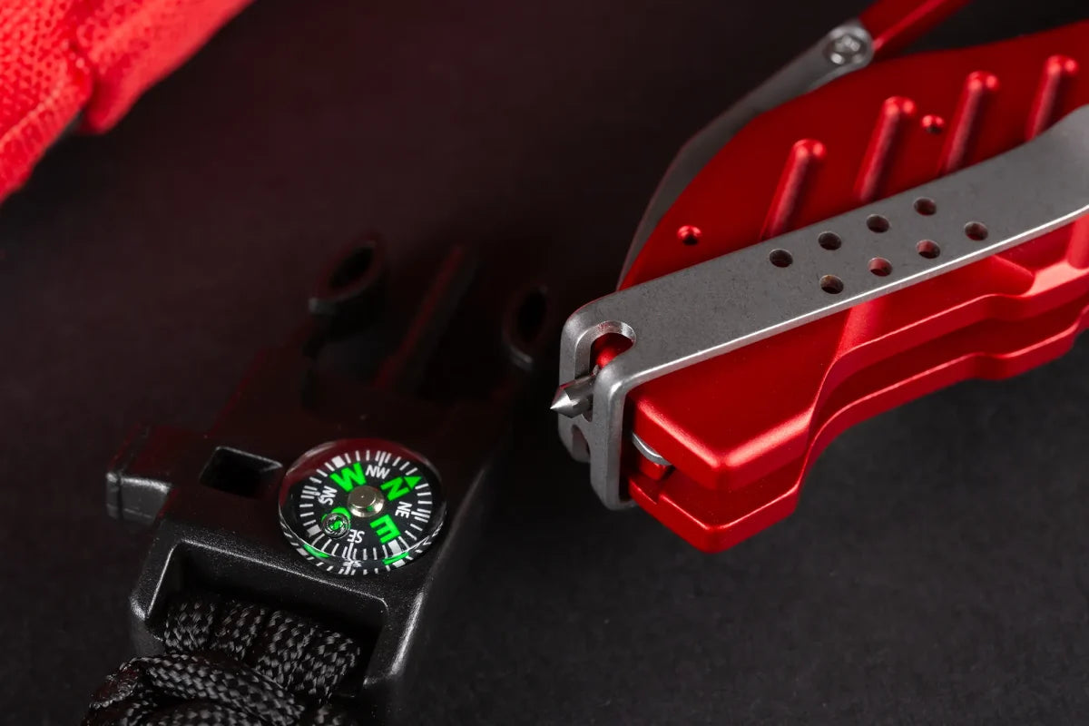 Eine Nahaufnahme eines roten Multitools mit silbernem Clip neben einem schwarzen Paracord-Armband mit grünem Kompass auf dunklem Hintergrund - perfekt für Fans der EXTREMA RATIO Extrema Ratio Messer Glauca G1 Rescue.