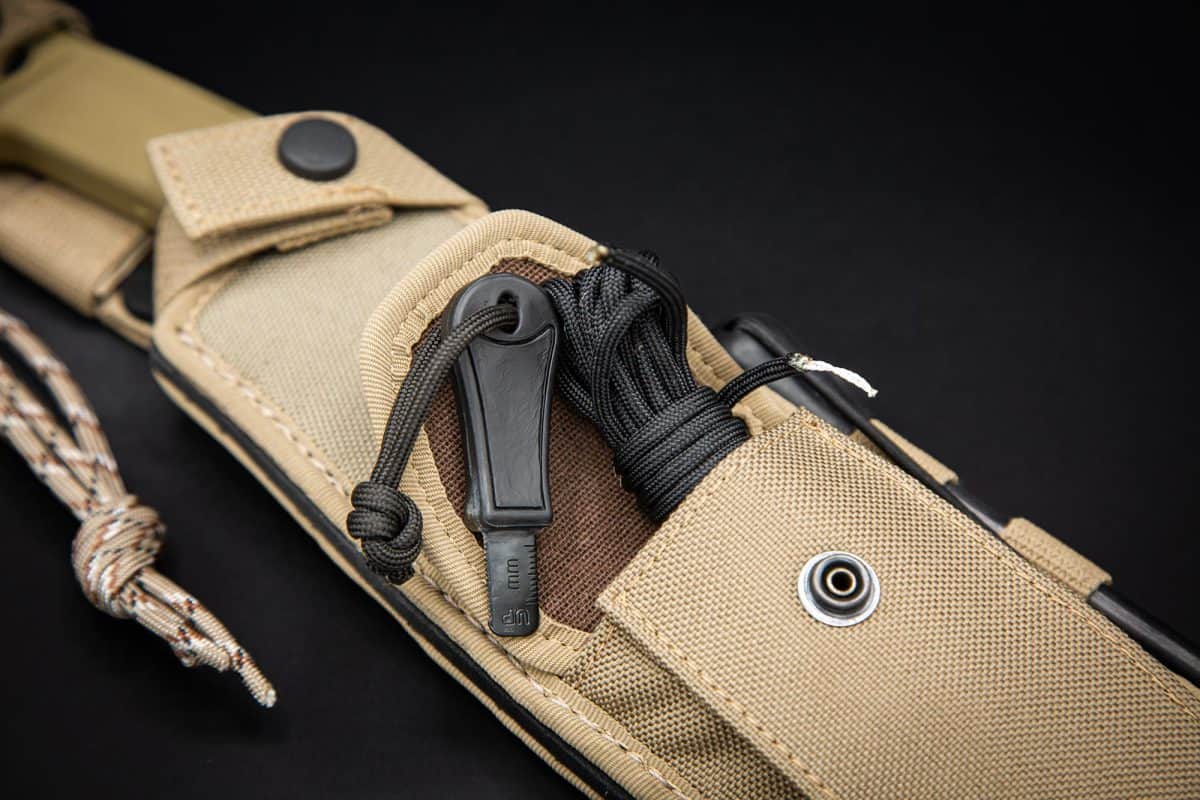 Nahaufnahme einer hellbraunen taktischen Scheide mit dem EXTREMA RATIO Extrema Ratio Messer Kreios Expedition, das mit Paracord befestigt ist, mit einer Druckknopftasche und robustem Material, dargestellt auf schwarzem Hintergrund.