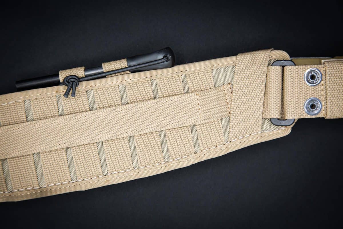 Nahaufnahme eines hellbraunen taktischen Gürtels mit verstärkten Nähten, Befestigungsschlaufen und Ösen, der ein EXTREMA RATIO Extrema Ratio Messer Kreios Expedition in einer schwarzen Scheide hält, vor einem dunklen Hintergrund.