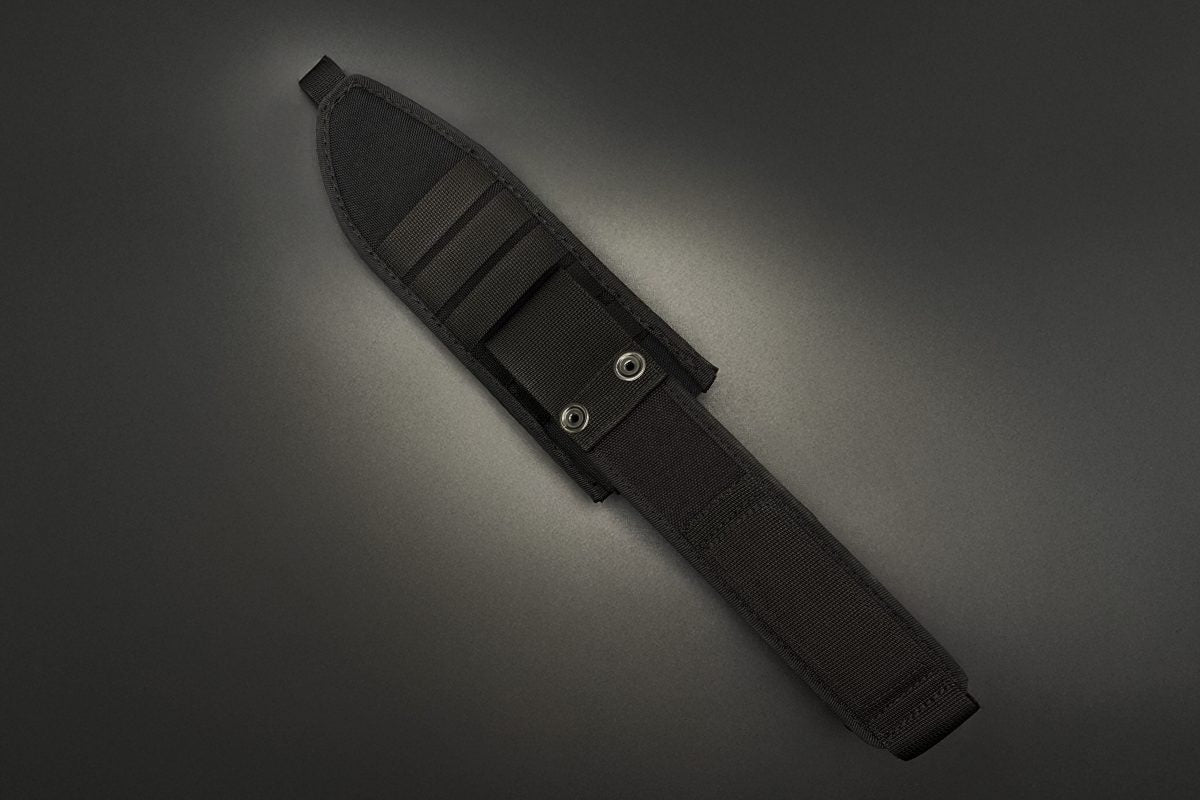 Schwarze Nylonscheide mit Gürtelschlaufe und Schnappverschluss, diagonal auf einem dunkelgrauen Hintergrund mit Spotlight-Effekt dargestellt. Entworfen für das EXTREMA RATIO Messer Numen S600 Black Überlebensmesser.