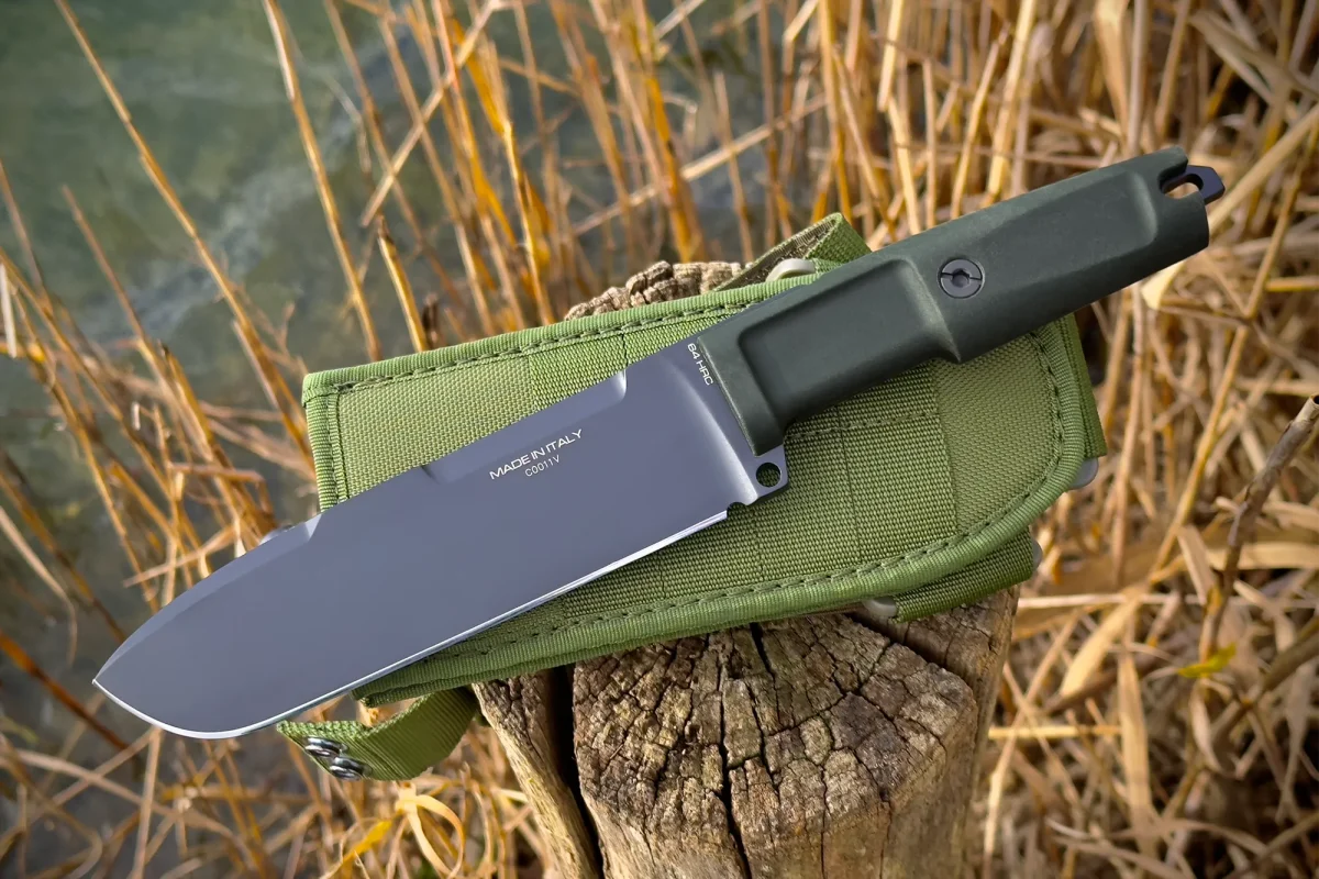Das EXTREMA RATIO Ontos II S600 Black ist ein in Italien hergestelltes Messer mit feststehender Klinge, schwarzem Griff und schwarzer Scheide, das auf einem Holzstumpf inmitten von getrocknetem Schilf in der Nähe von Wasser liegt.