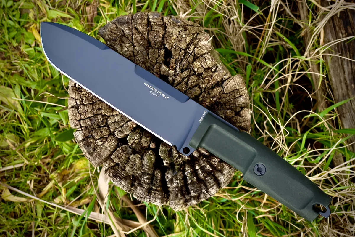 Das Extrema Ratio Messer Ontos II S600 Black von EXTREMA RATIO mit grünem Griff und dunkler Klinge mit der Aufschrift "MADE IN ITALY" ruht auf einem verwitterten Baumstumpf inmitten von Gras und Blättern.