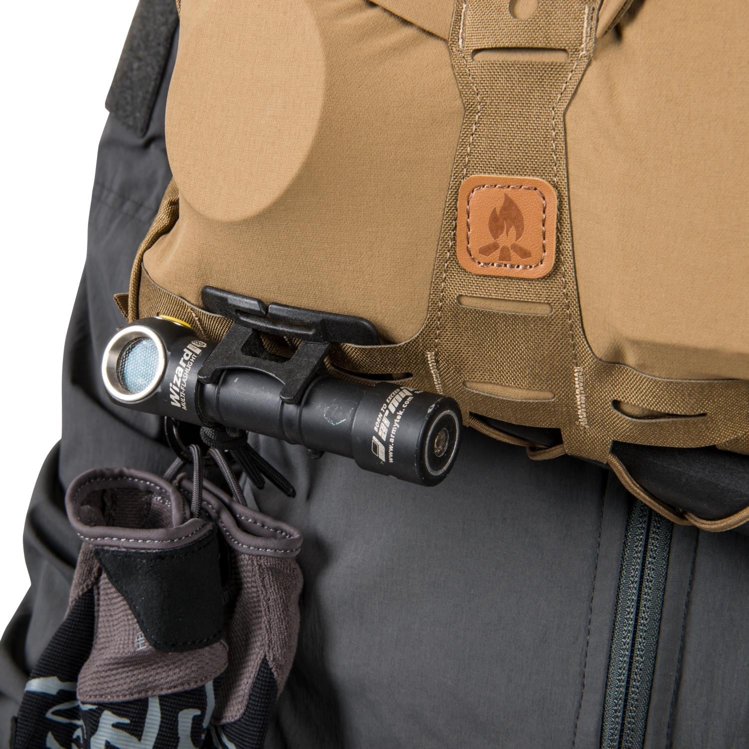 Eine Armytek Wizard-Multitaschenlampe ist an einer HELIKON-TEX Chest Pack Numbat® in Earth Brown / Clay B befestigt, die mit einem Lagerfeuer-Logoaufnäher aus Leder versehen ist, und wird mit einer dunklen Hose und Handschuhen kombiniert.