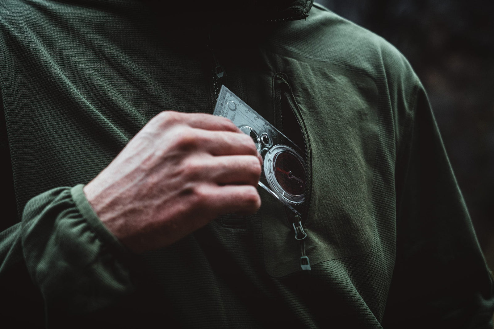 Bekleidet mit einem HIGHLANDER FORCES Tactical Hirta Fleece - Coyote Tan, zieht eine Person einen durchsichtigen Kompass aus ihrer Brusttasche, der auf die Navigation im Freien hinweist.