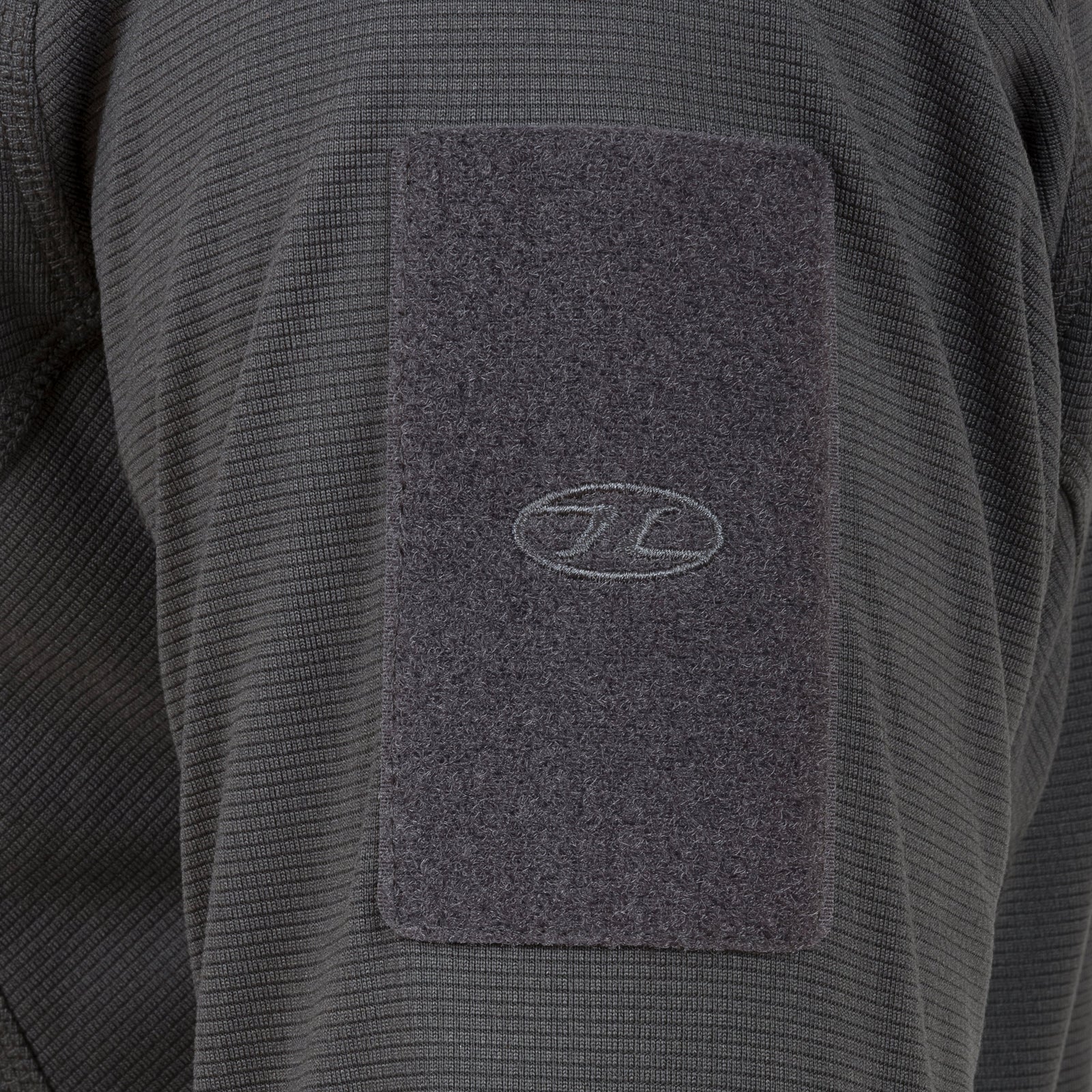 Eine Nahaufnahme des HIGHLANDER FORCES Tactical Hirta Fleece - Dark Grey zeigt ein ovales Logo-Patch auf dem Ärmel dieses strukturierten taktischen Kleidungsstücks.