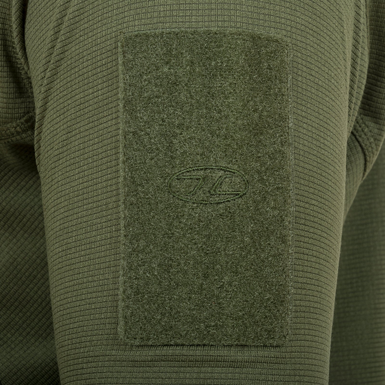 Nahaufnahme eines Highlander Forces Tactical Hirta Fleece-Ärmels in Olivgrün mit einem rechteckigen Aufnäher mit einem gestickten ovalen Logo in der Mitte, der das funktionelle Design des HIGHLANDER FORCES-Kleidungsstücks unterstreicht.