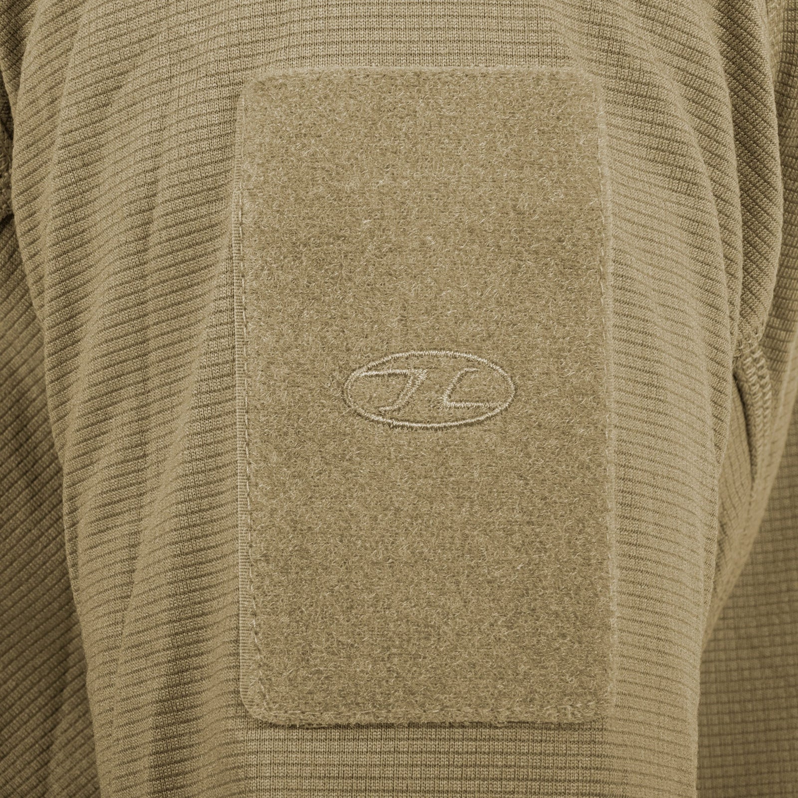 Nahaufnahme eines strukturierten, hellbraunen Stoffaufnähers mit einem ovalen, in der Mitte aufgenähten Logo, der an einem HIGHLANDER FORCES Tactical Hirta Fleece in Ranger Green befestigt ist.