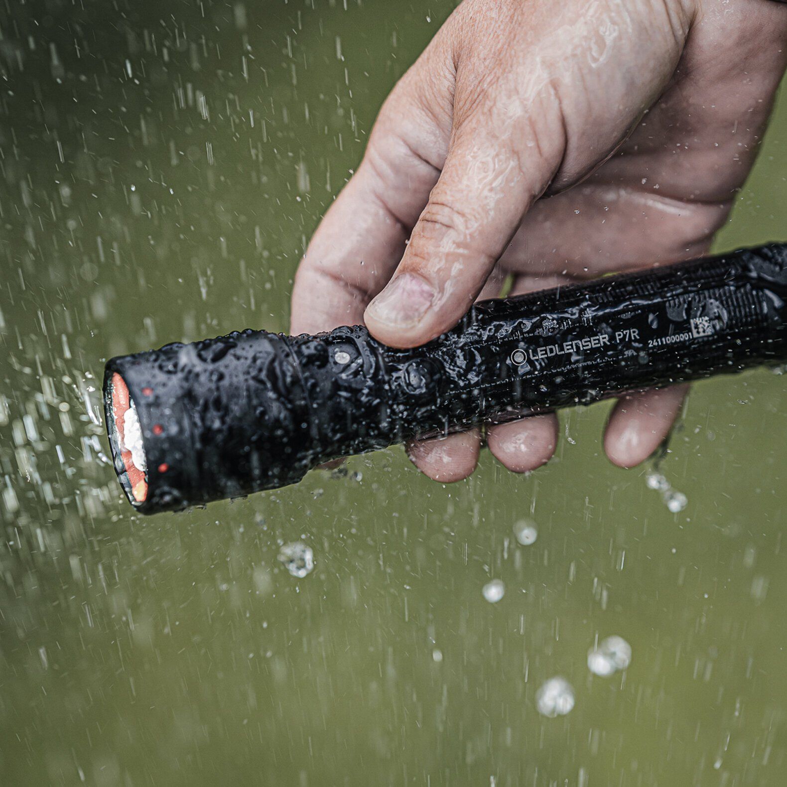 Eine Hand hält die LEDLENSER Taschenlampe P7R im Freien, während Wasser über den hellen 2000-Lumen-Strahl spritzt und die Wasserfestigkeit und die leistungsstarke LED-Beleuchtung der Taschenlampe hervorhebt.