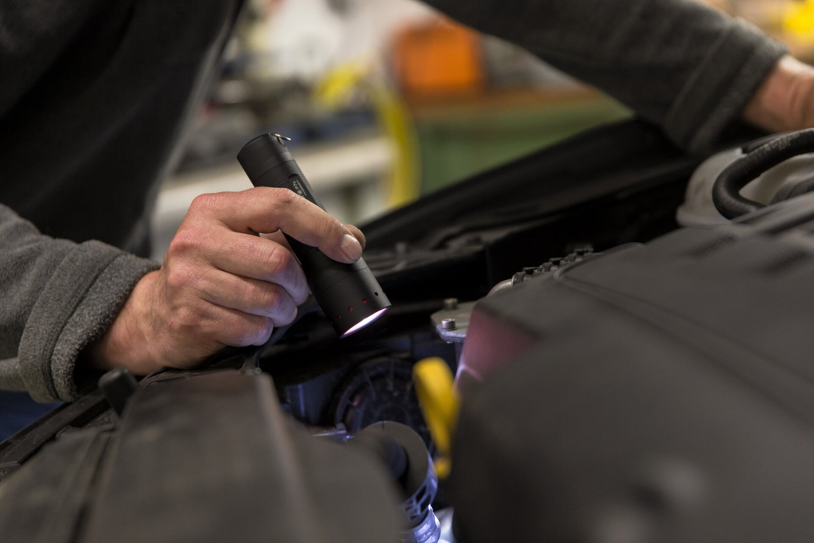 Eine Person benutzt eine LEDLENSER Taschenlampe P7, um einen Automotor zu inspizieren. Sie hält die Taschenlampe in einer Hand und arbeitet unter der Motorhaube.