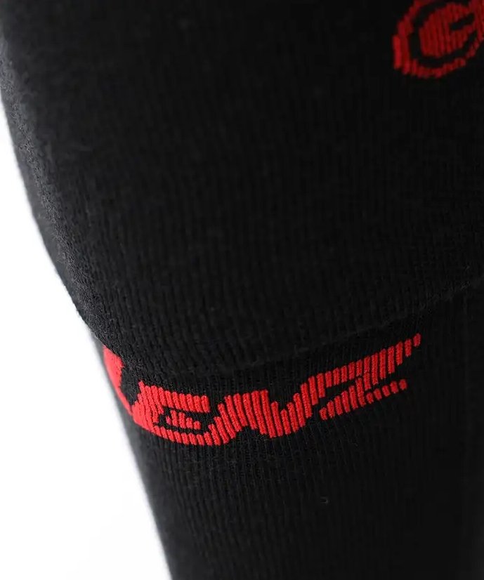 Nahaufnahme von schwarzem Stoff, wahrscheinlich von LENZ Heizsocken 6.1 Toe Cap Merino Compression Socken, mit rotem, teilweise sichtbarem stilisiertem Text oder Logo. Der Hintergrund ist einfarbig weiß.