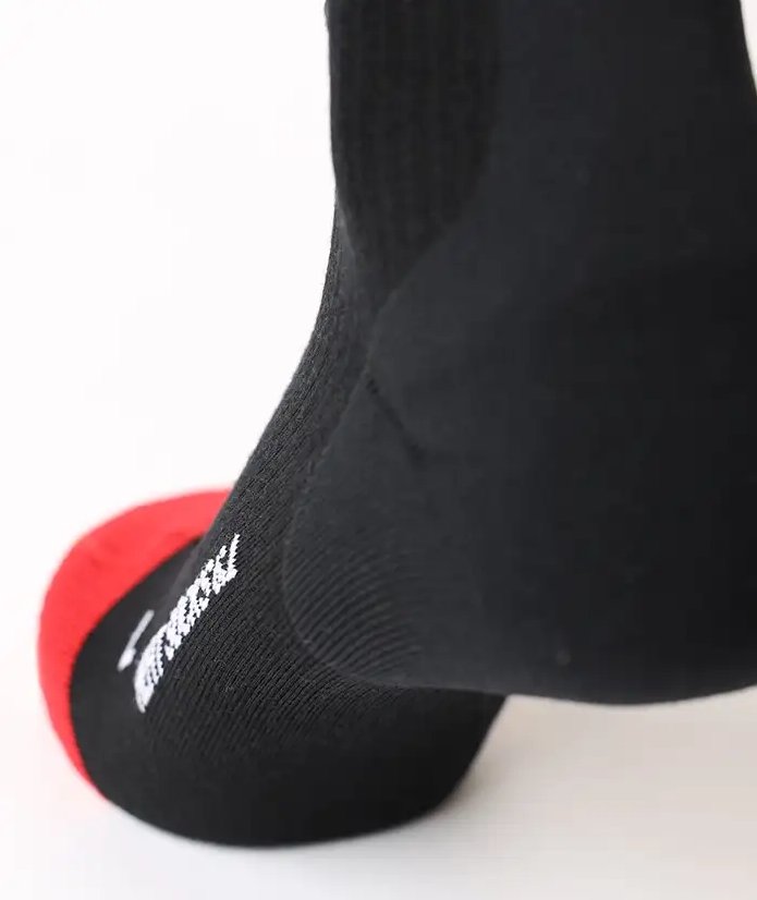 Nahaufnahme eines Fußes, der die LENZ Lenz Heizsocken 6.1 Toe Cap Merino Compression Socken mit roter Spitze und weißem Seitentext auf einer weißen Fläche trägt.
