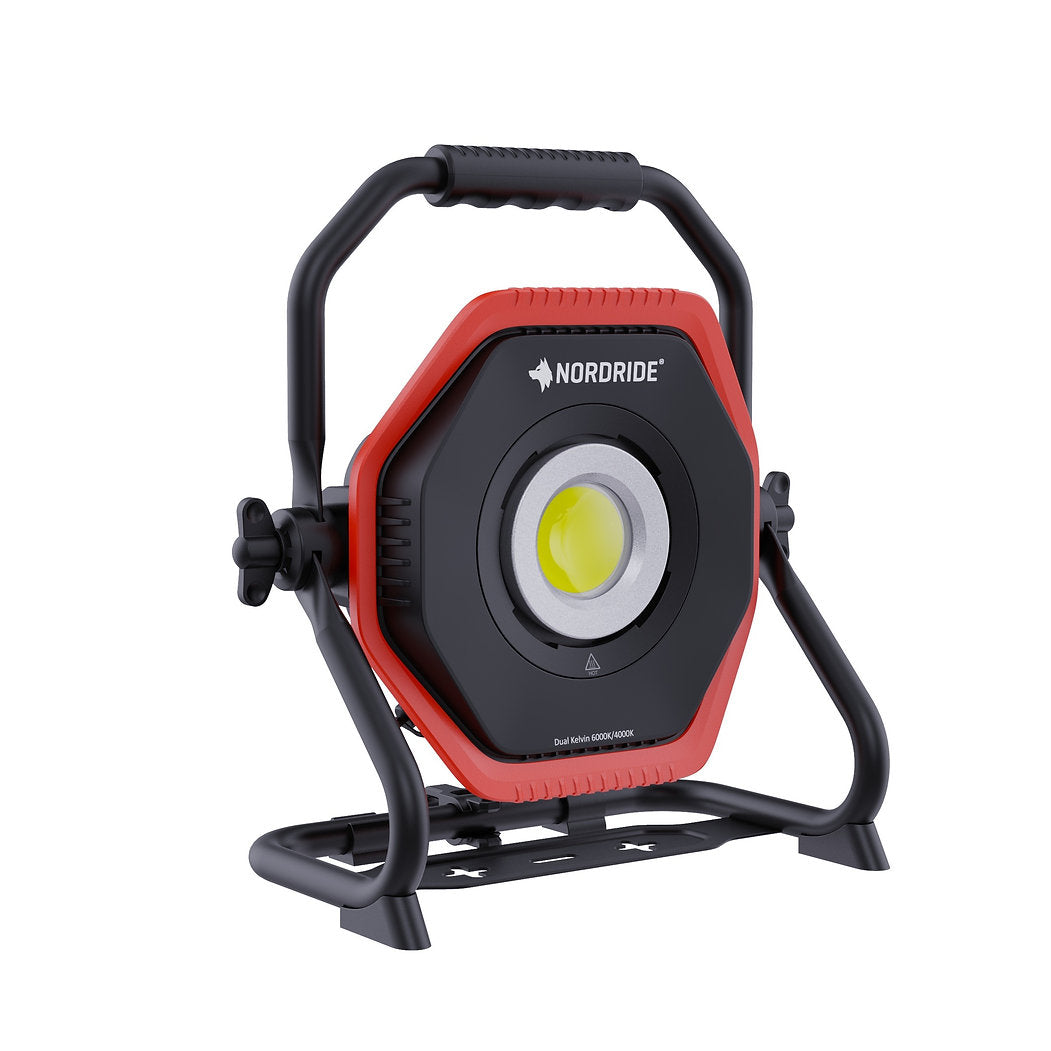 Der NORDRIDE Hochleistungsstrahler Lumos 80W R Dual Kelvin ist eine tragbare LED-Leuchte mit schwarz-rotem, sechseckigem Gehäuse, stabilem Standfuß und Griff - ideal für die Baustellenbeleuchtung. Die Marke NORDRIDE ist oberhalb der Leuchte aufgedruckt.