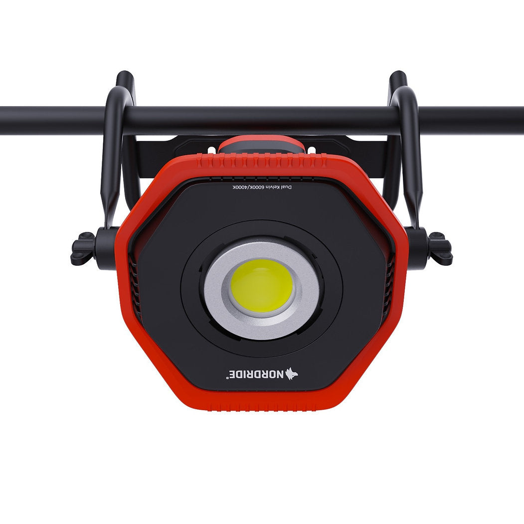 Eine Nahaufnahme des NORDRIDE Nordride Hochleistungsstrahler Lumos 80W R Dual Kelvin LED Arbeitsscheinwerfer, rot und schwarz, montiert mit verstellbaren Klemmen an einer schwarzen Metallstange - perfekt für präzise Baustellenbeleuchtung.