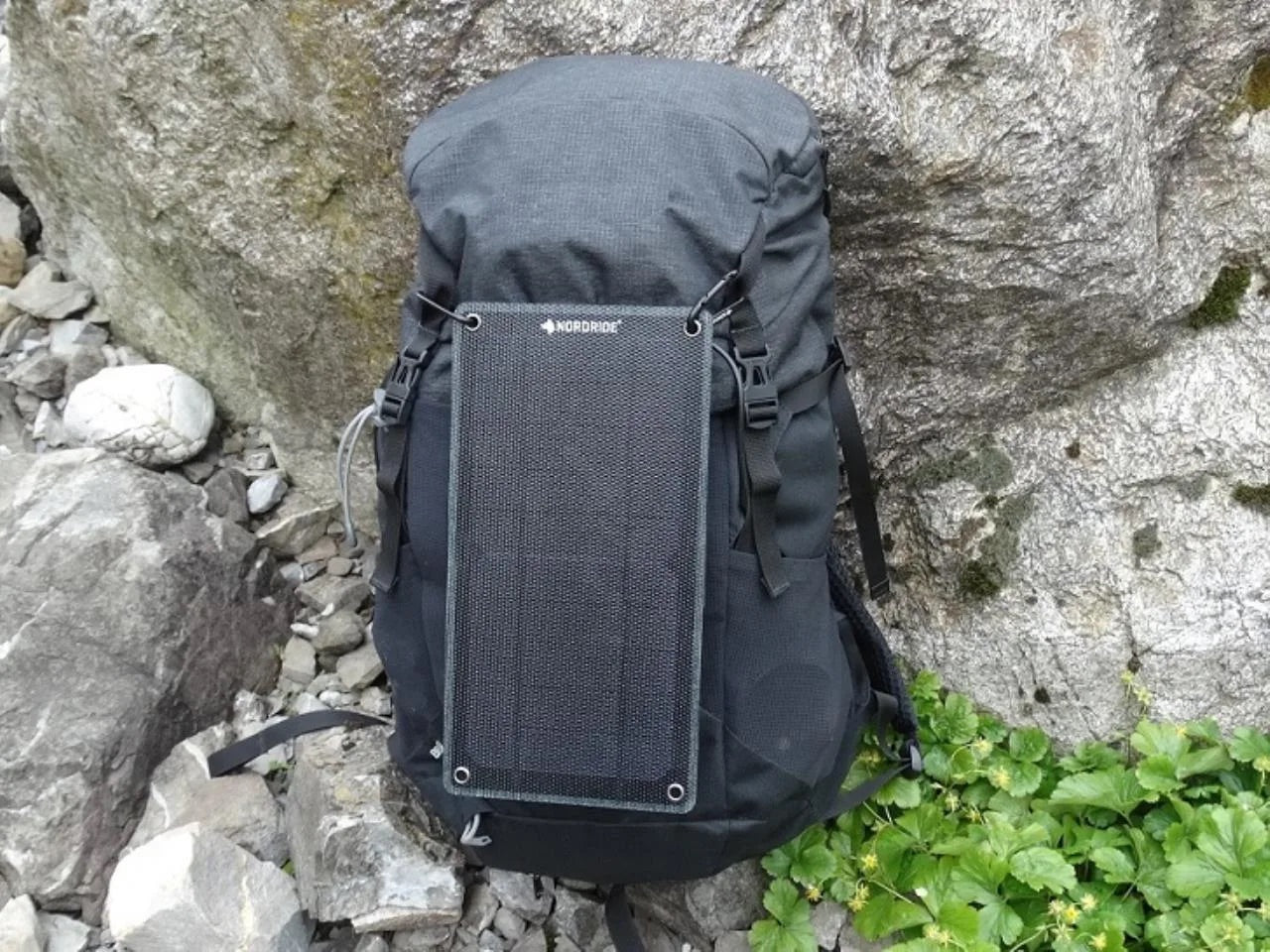 Der NORDRIDE SOLAR PULSE 7W Rucksack mit mobilem Ladegerät sitzt auf einem Felsen und ist bereit, die Energie der Sonne für all Ihre Abenteuer zu nutzen.