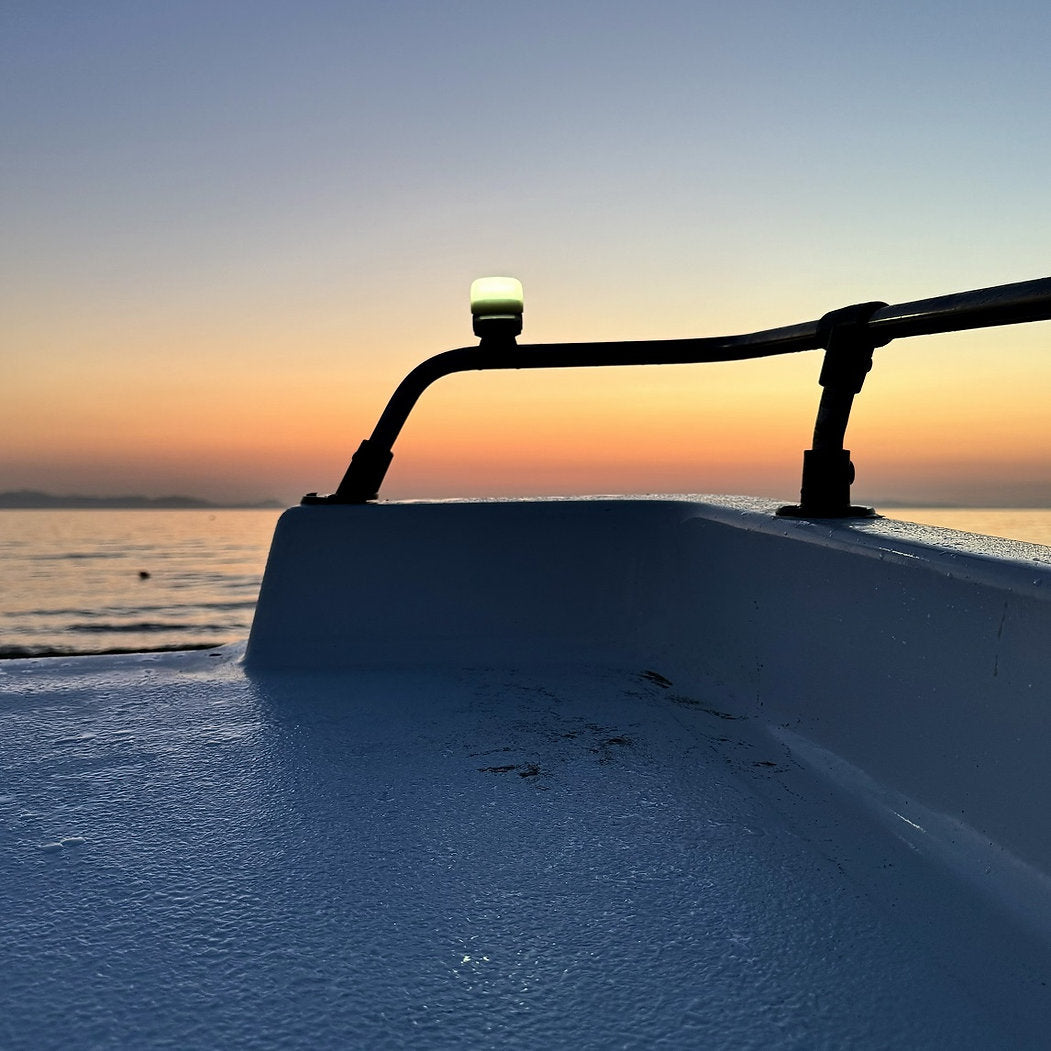 Nahaufnahme von einem Boot auf dem Meer während des Sonnenuntergangs, mit sanften orangefarbenen und blauen Farbtönen. Eine NORDRIDE Signalkappe & Diffusor zu Scout, Patrol & Paramedic Light leuchtet sanft und beleuchtet die Szene, während sich die Wellen im Hintergrund bewegen.
