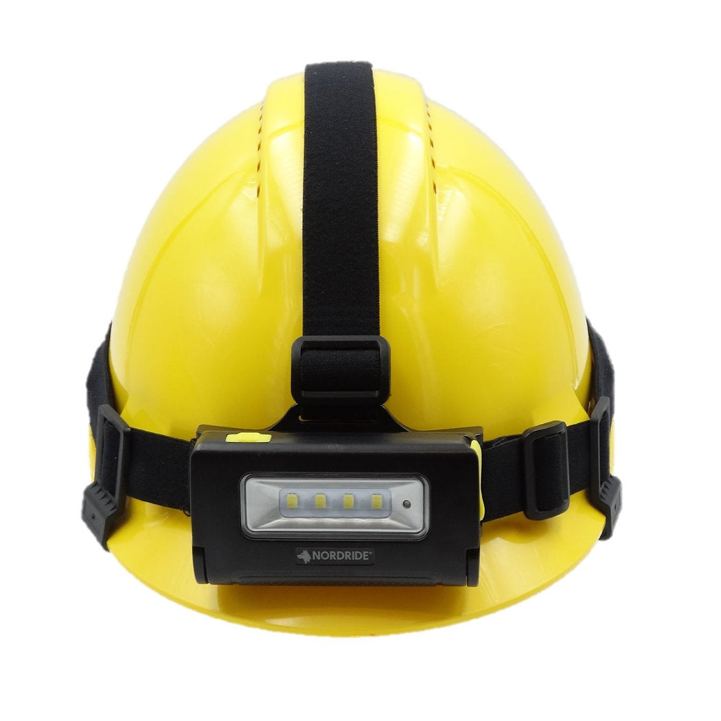 Ein gelber Schutzhelm mit einem schwarzen Riemen und einer NORDRIDE Nordride Stirnlampe Duo auf der Vorderseite. Diese Stirnlampe verfügt über vier kleine Lichter für freihändiges Arbeiten und sitzt sicher auf dem Helm.