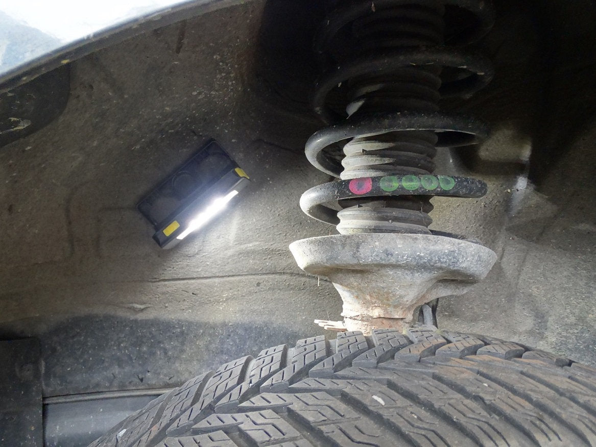 Nahaufnahme des Radkastens eines Autos mit einem Reifen, einer Schraubenfeder und einem Federbein. Eine NORDRIDE Nordride Strinlampe Duo ist innen angebracht und leuchtet den Bereich für Inspektion oder Reparatur hell aus.