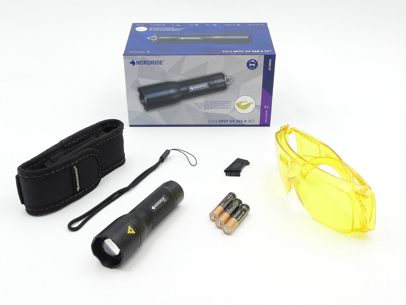 Das NORDRIDE Nordride Taschenlampe Spot UV 365 A Set besteht aus einer UV-Taschenlampe, einem schwarzen Nylonholster, einer gelben Schutzbrille, AAA-Batterien, einem Pinselzubehör und einer Verpackungsbox.