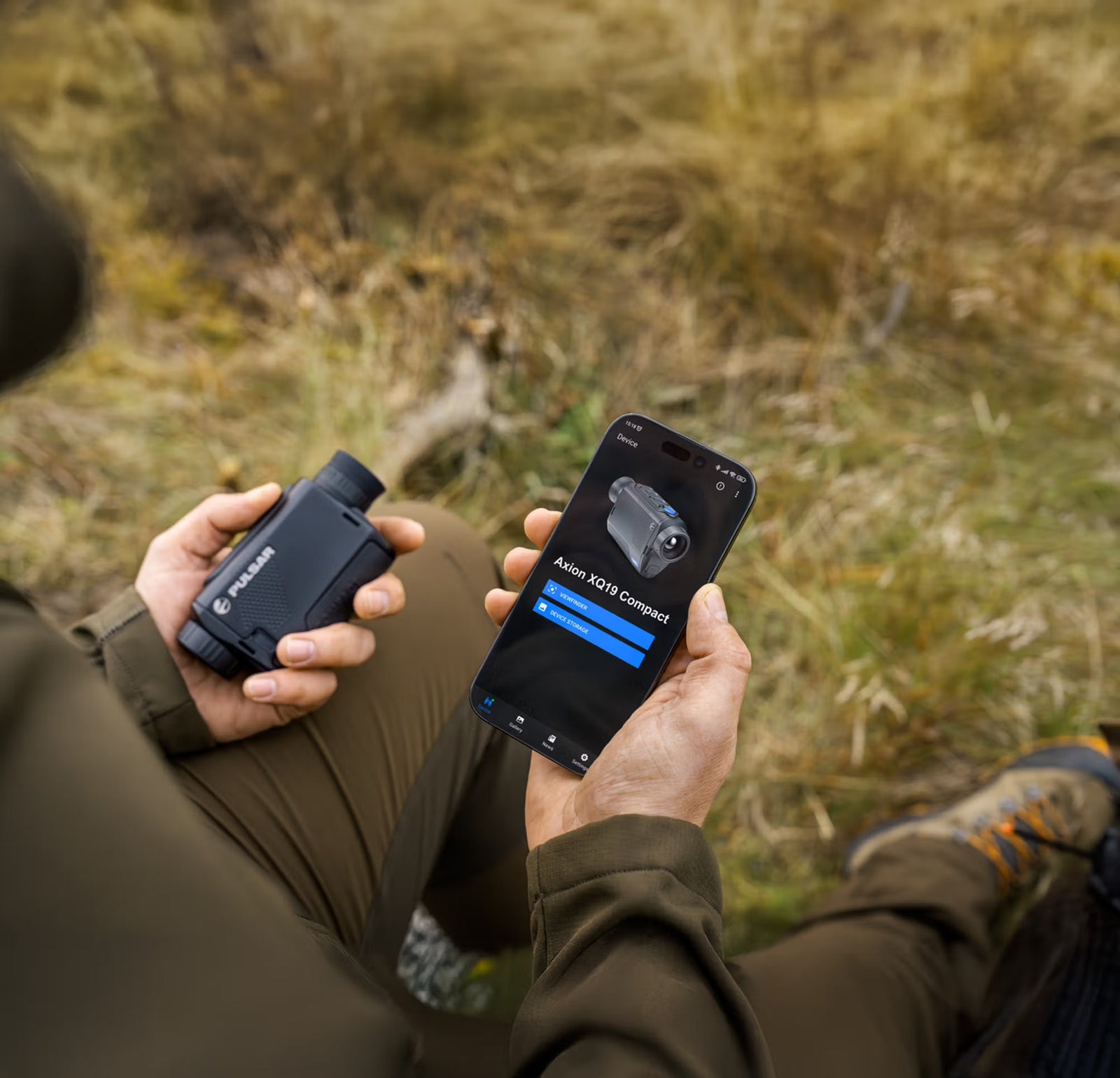 Eine Person im Freien auf grasbewachsenem Gelände hält ein PULSAR Wärmebildgerät Axion XQ19 Compact in der einen und ein Smartphone in der anderen Hand, auf dem eine App mit Fernglasbildern und Produktdetails angezeigt wird.