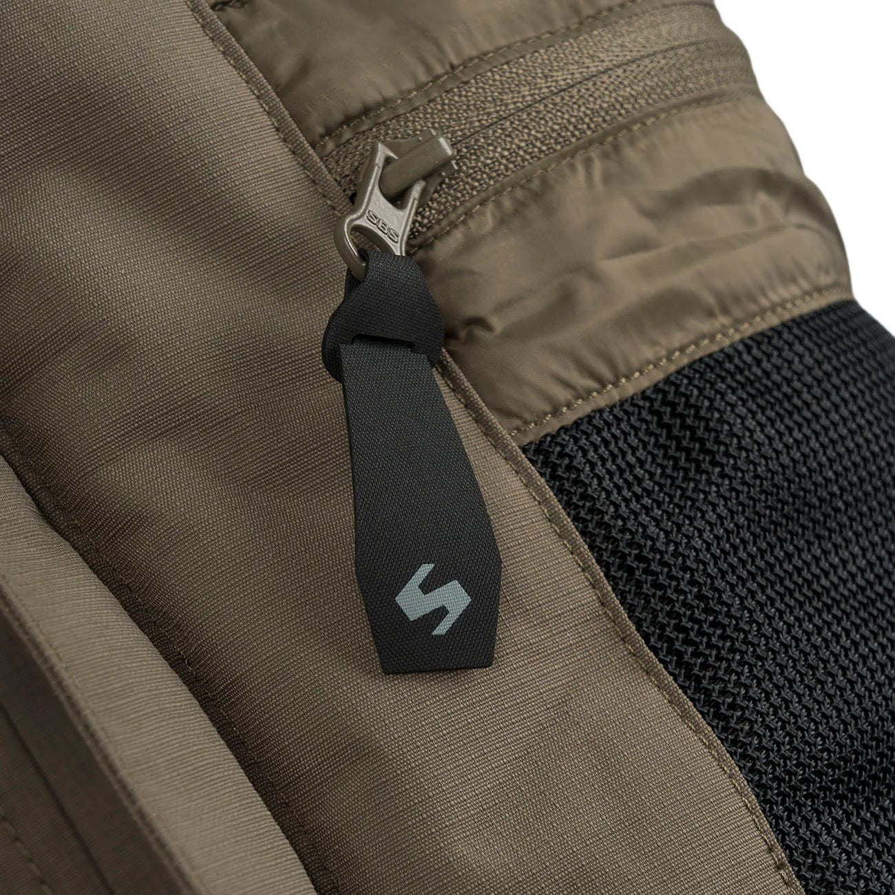 Nahaufnahme eines braunen Stoffbeutels mit Reißverschlusstasche, seitlichem Netzeinsatz und schwarzer Lasche mit grauem S-Logo - ideal zur STOIRM Primaloft® Winter Jacket - Ranger Green oder einer anderen wasserdichten Jacke von STOIRM.