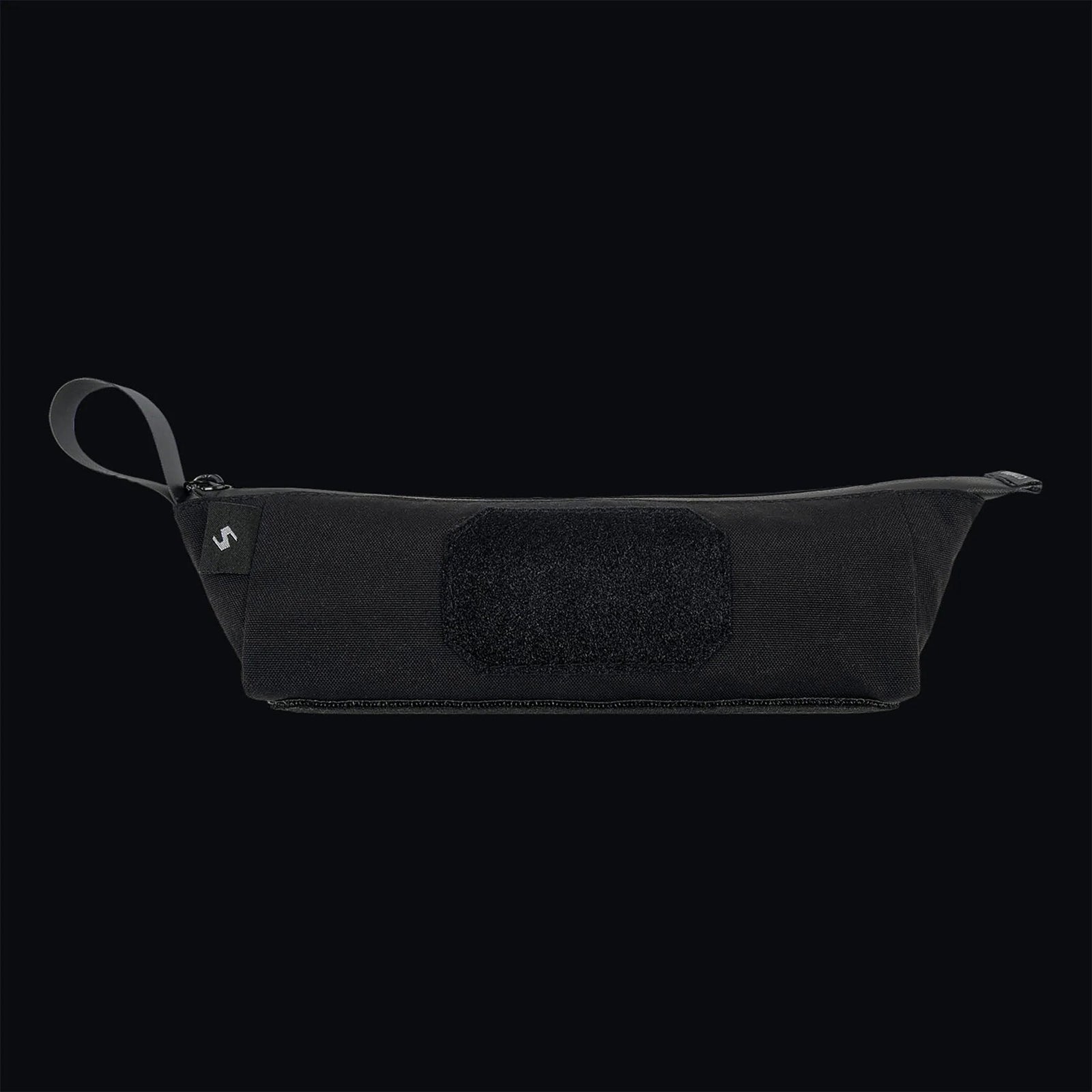 Die STOIRM Utility Pouch von STOIRM ist eine schwarze, wasserdichte Tasche mit Reißverschluss, einem Griff aus Stoff auf der linken Seite und einem rechteckigen Klettverschluss auf der Vorderseite, der auf einem schlichten dunklen Hintergrund abgebildet ist.