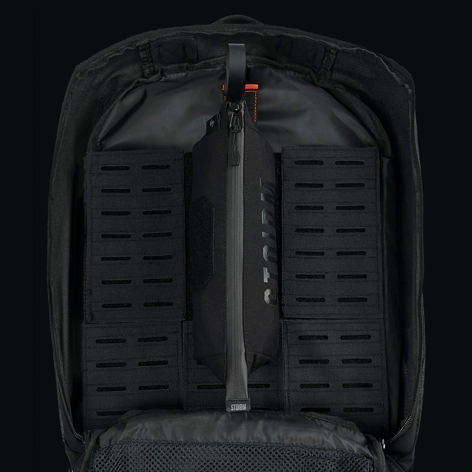 Der schwarze Rucksack lässt sich öffnen und bietet einen organisierten Innenraum mit modularen Paneelen, einer sicheren vertikalen Reißverschlusstasche mit der Aufschrift STOIRM Utility Pouch und einer Netztasche am Boden. Die abnehmbare Tasche sorgt für Flexibilität und unterstreicht die taktische Strapazierfähigkeit von STOIRM.