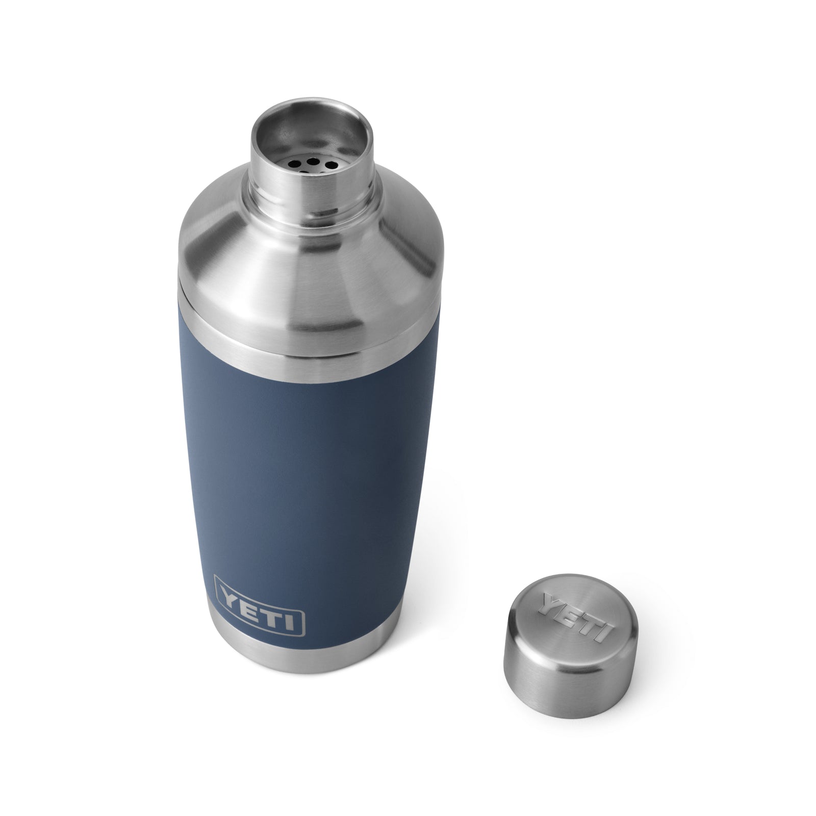 Der YETI® Cocktail-Shaker 20 Oz - Navy aus 18/8-Edelstahl mit doppelwandiger Vakuumisolierung steht auf weißem Hintergrund, der passende Deckel der Marke YETI liegt rechts daneben.