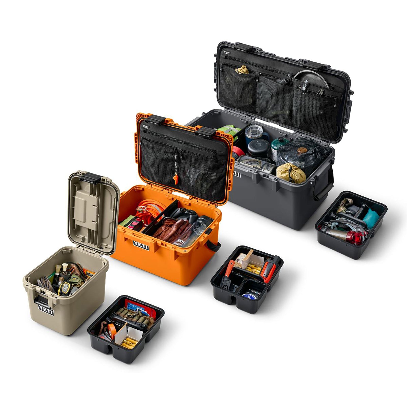 Drei offene YETI LoadOut GoBox-Einheiten in Orange, Hellbraun und Anthrazit sind mit Ausrüstung und Zubehör bepackt, daneben stehen mehrere schwarze YETI® Einlegekörbe zu LoadOut GoBox-Organisationstabletts, alle auf weißem Hintergrund.