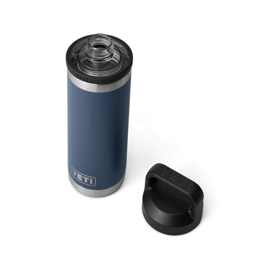 Eine YETI® Flasche Rambler 18 Oz - Navy mit doppelwandiger Vakuumisolierung steht auf einem weißen Hintergrund, dessen silberner Boden glänzt. Daneben liegt der schwarze Chug Cap Deckel, der offene Hals zeigt das leere Innere.