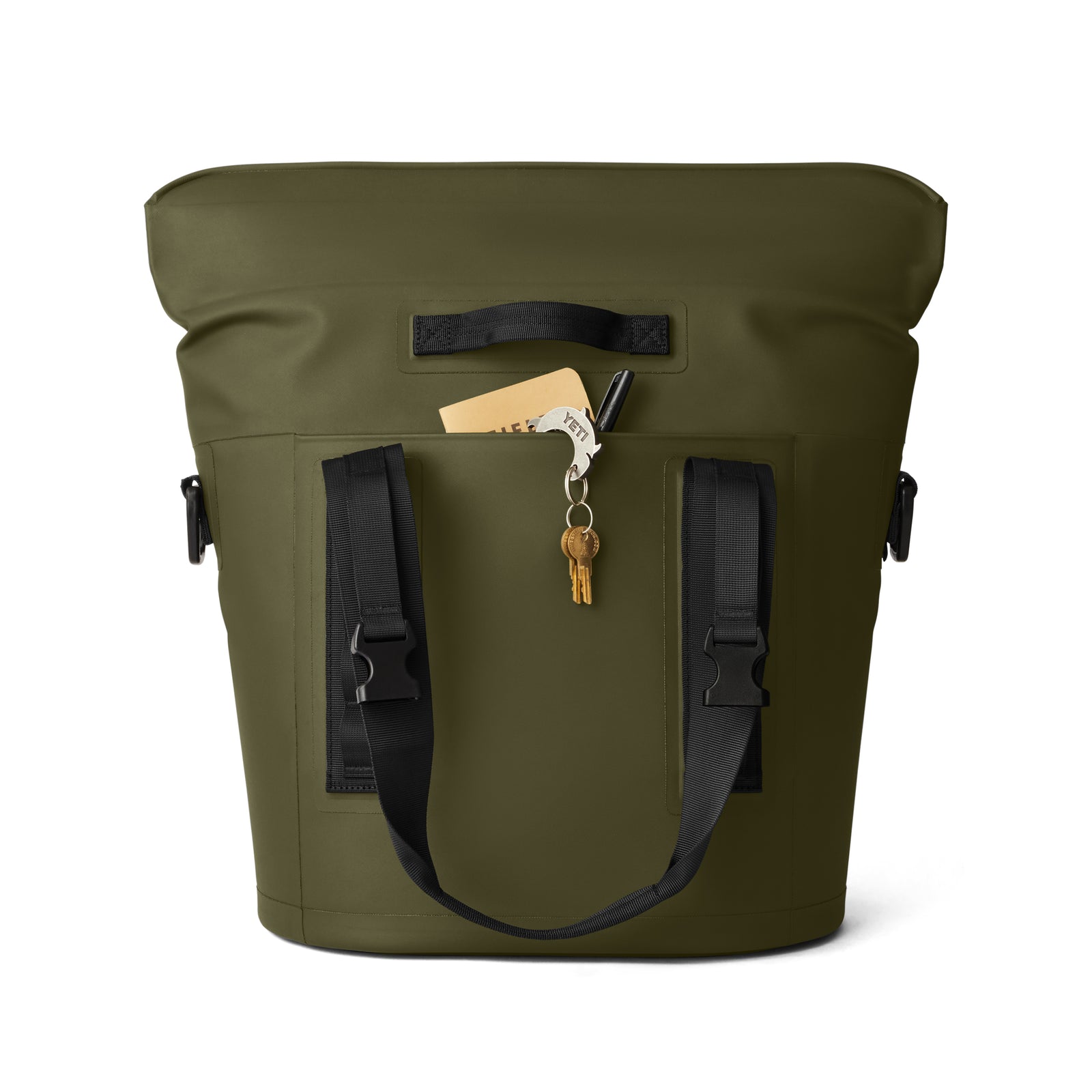Eine olivgrüne YETI® Hopper M15 Soft Cooler mit schwarzen Gurten und einer Vordertasche, in der ein Stift, Schlüssel und gefaltetes Papier Platz finden, vor einem weißen Hintergrund.
