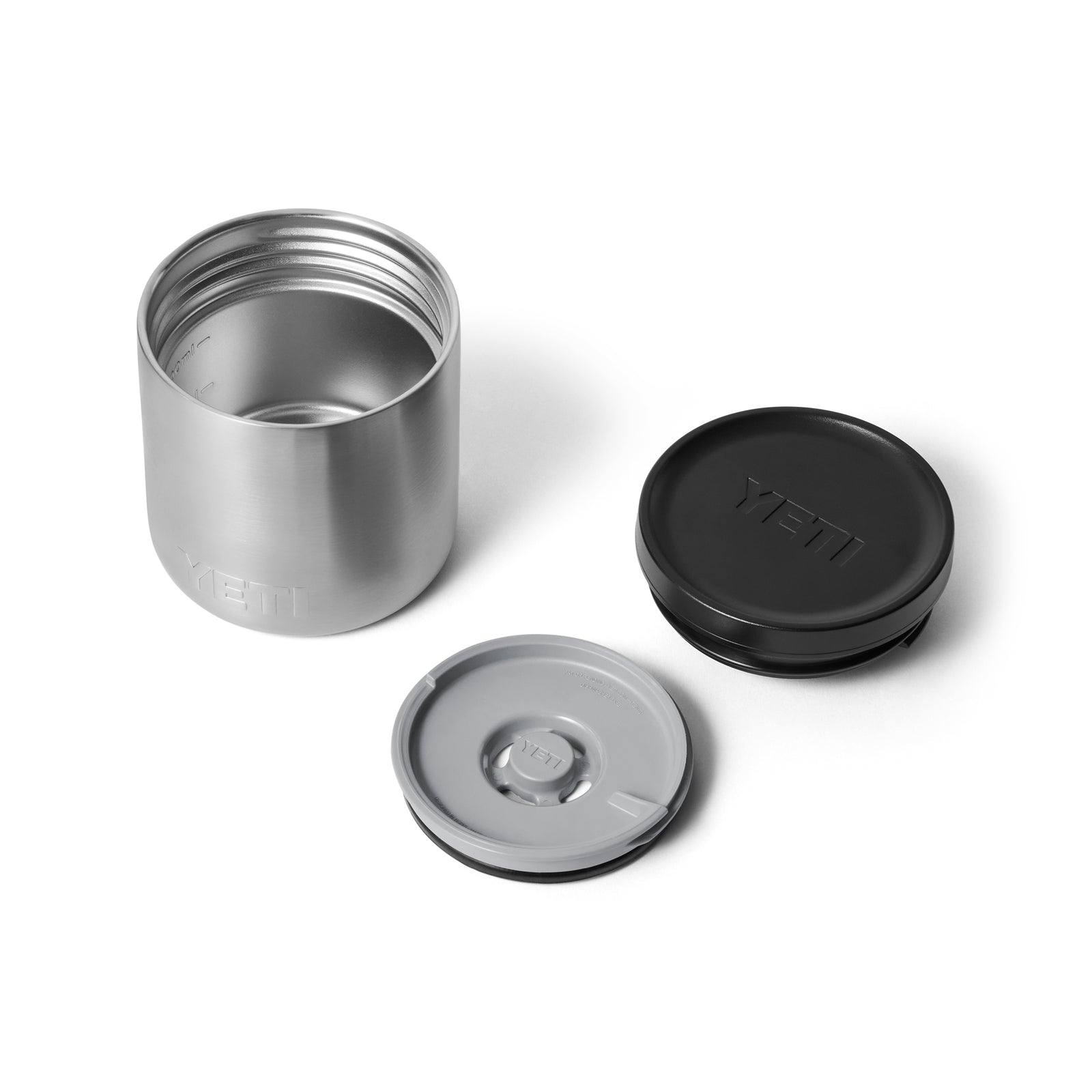 Ein YETI® Isolierter Essensbehälter Rambler 8 oz - Stainless Steel mit abgenommenen schwarzen und grauen Deckeln auf weißem Hintergrund daneben.