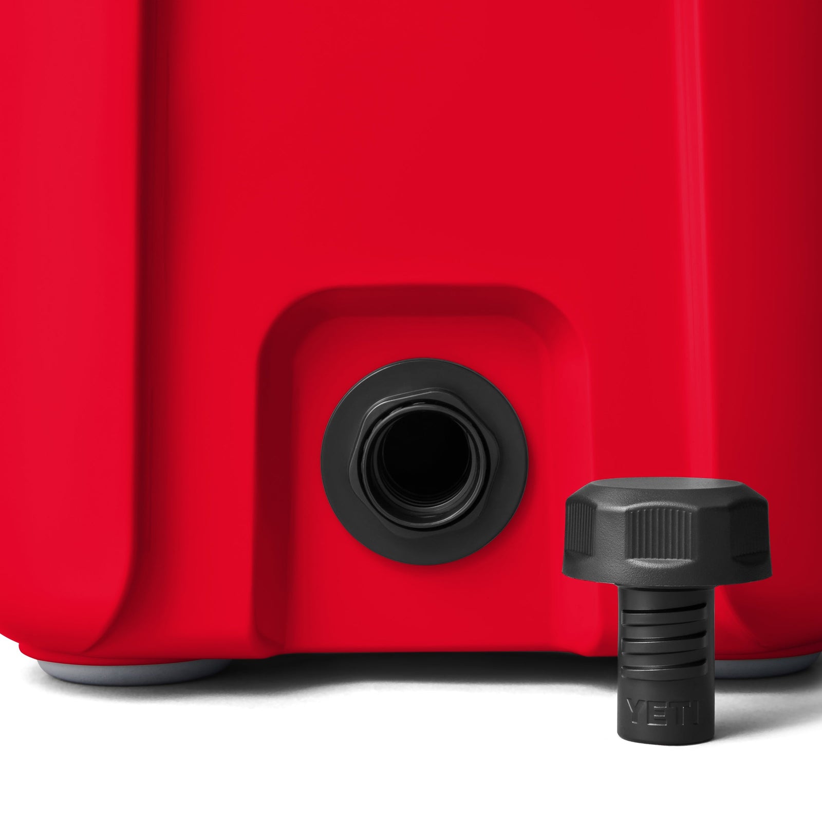 Nahaufnahme der unteren Ecke einer YETI® Kühlbox Roadie 15 - Rescue Red mit schwarzem Schraubdeckel vor einem offenen Gewindeauslauf. Das YETI-Logo ist auf dem Deckel eingeprägt.
