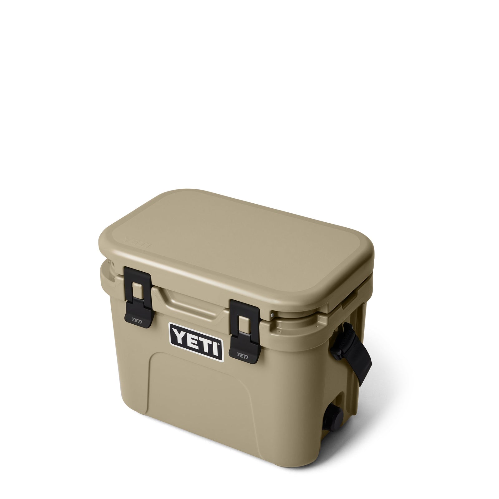 Die YETI® Kühlbox Roadie 15 - Tan hat ein rechteckiges Design mit schwarzen Seitengriffen und Frontverschlüssen auf weißem Hintergrund. Das YETI-Logo ist auf der Vorderseite der Kühlbox sichtbar.