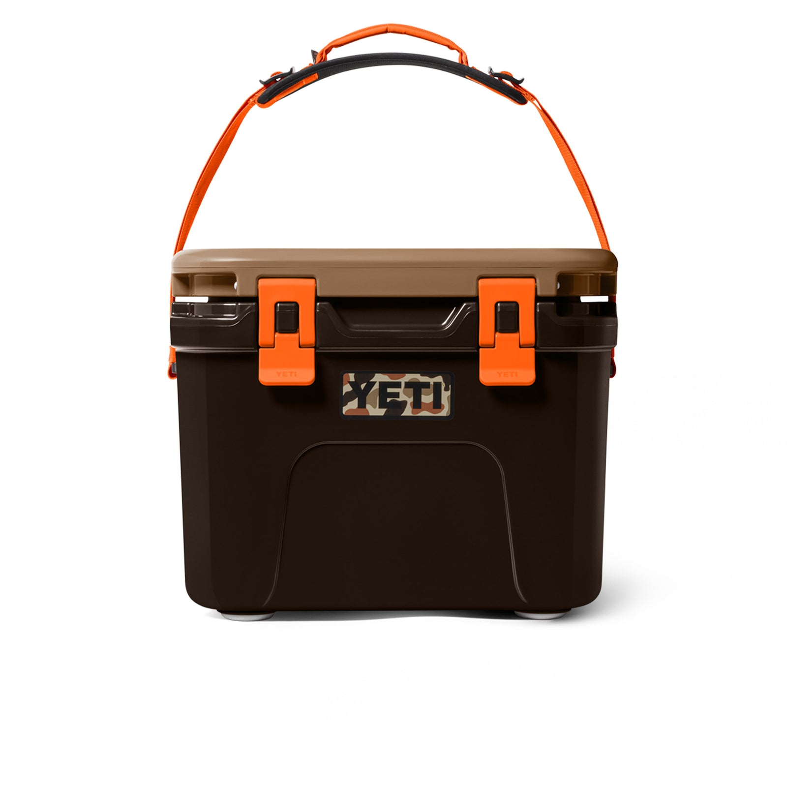 Die YETI® Kühlbox Roadie 15 - Wetlands Camo hat einen dunkelbraunen Körper, einen hellbraunen Deckel, orangefarbene Verschlüsse und einen orangefarbenen Trageriemen auf weißem Hintergrund.