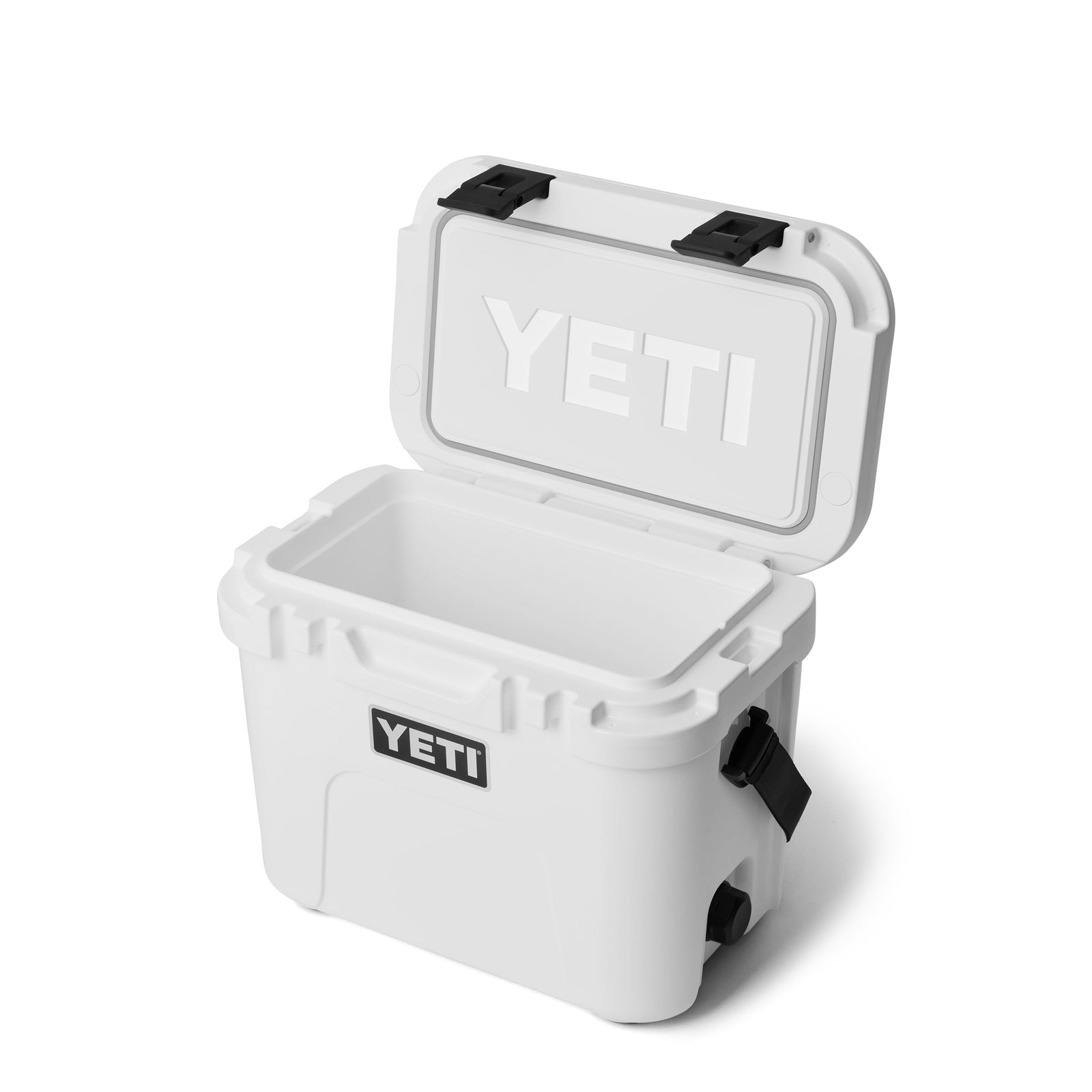Die YETI® Kühlbox Roadie 15 - White wird mit einem schwarzen Riegel geöffnet und offenbart ihren leeren Innenraum und das sichtbare YETI-Logo auf der Vorder- und Deckelunterseite. Sie steht vor einem schlichten weißen Hintergrund - ideal für eine mobile Kühlbox.