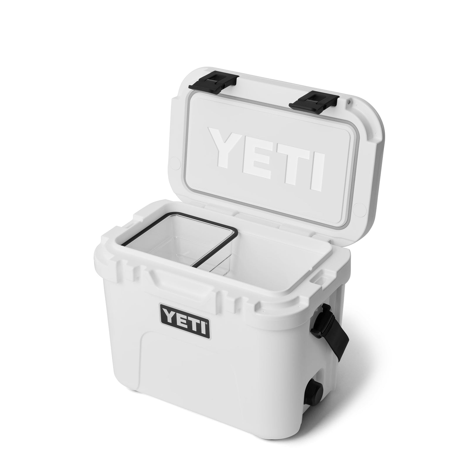 Eine weiße YETI® Kühlbox Roadie 15 mit schwarzen Griffen und Verschlüssen hat einen offenen Deckel mit einem rechteckigen Korbeinsatz. Der Markenname YETI steht auf der Vorderseite und auf der Innenseite des Deckels.