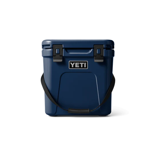 Die YETI® Kühlbox Roadie 24 in Navy mit schwarzer PermaFrost Isolierung, einem schwarzen Schultergurt, zwei schwarzen Deckelverschlüssen und dem YETI-Logo auf der Vorderseite ist auf weißem Hintergrund abgebildet.