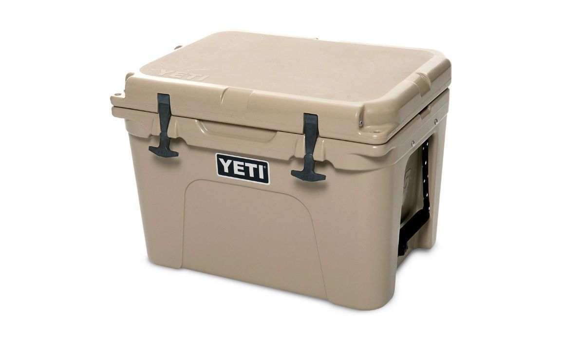 Die YETI® Kühlbox Tundra 35 - Tan hat eine robuste Konstruktion, seitliche Griffe, schwarze Gummiverschlüsse und das YETI-Logo - ideal als robuste Kühlbox für jedes Campingabenteuer.