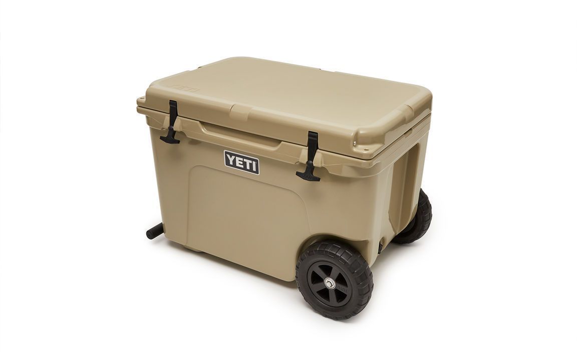 Die YETI® Kühlbox Tundra Haul - Tan mit Klappdeckel, schwarzen Griffen, zwei großen schwarzen Rädern und Ablaufventil ist vor weißem Hintergrund abgebildet.