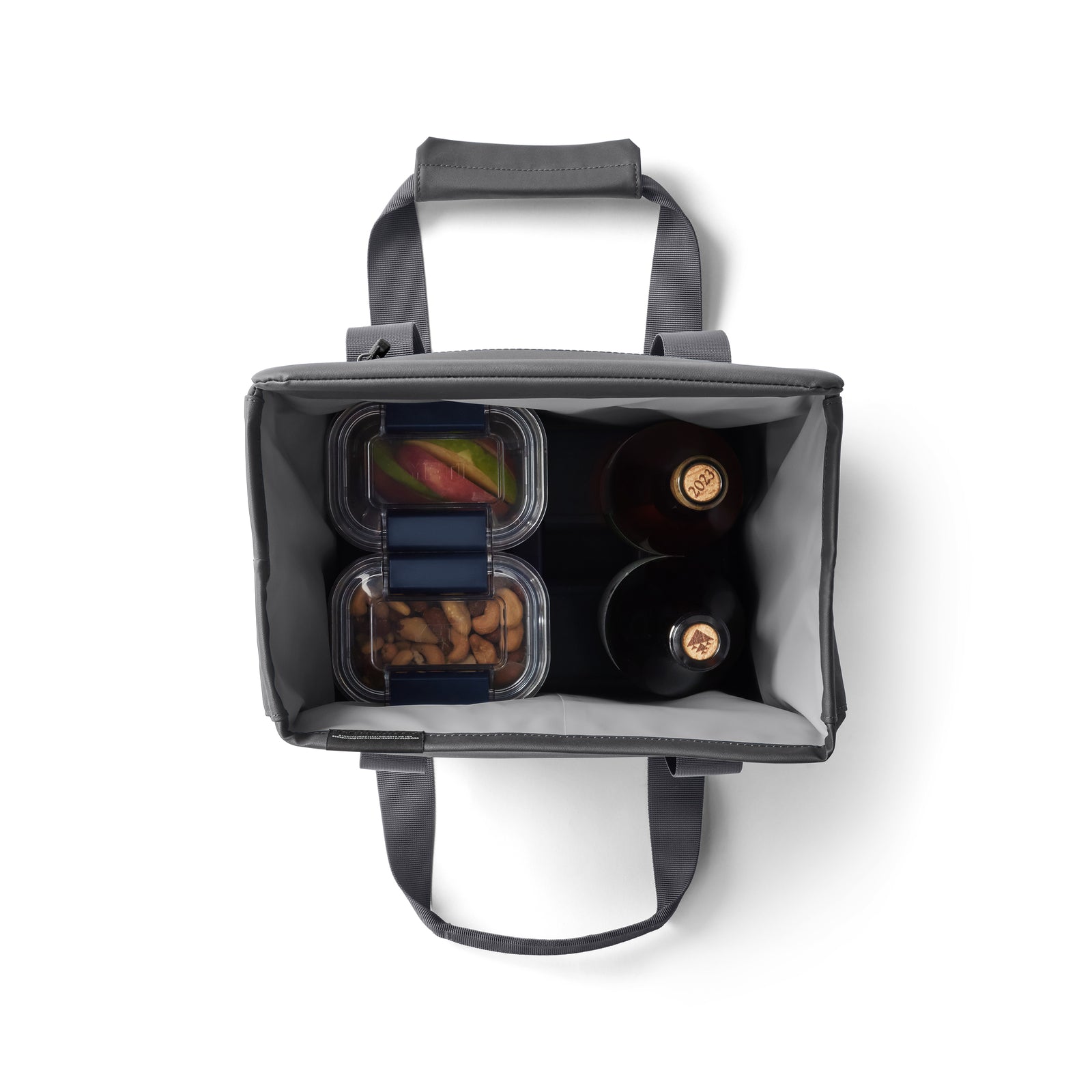 Draufsicht auf eine geöffnete YETI® Kühltasche Daytrip Lunch Bag 14L - Charcoal mit zwei Flaschen, gemischtem Obst und Mandeln. Diese YETI Tasche hat Coldcell Flex Isolierung, sowie kurze Griffe und einen Schultergurt für einfaches Tragen.
