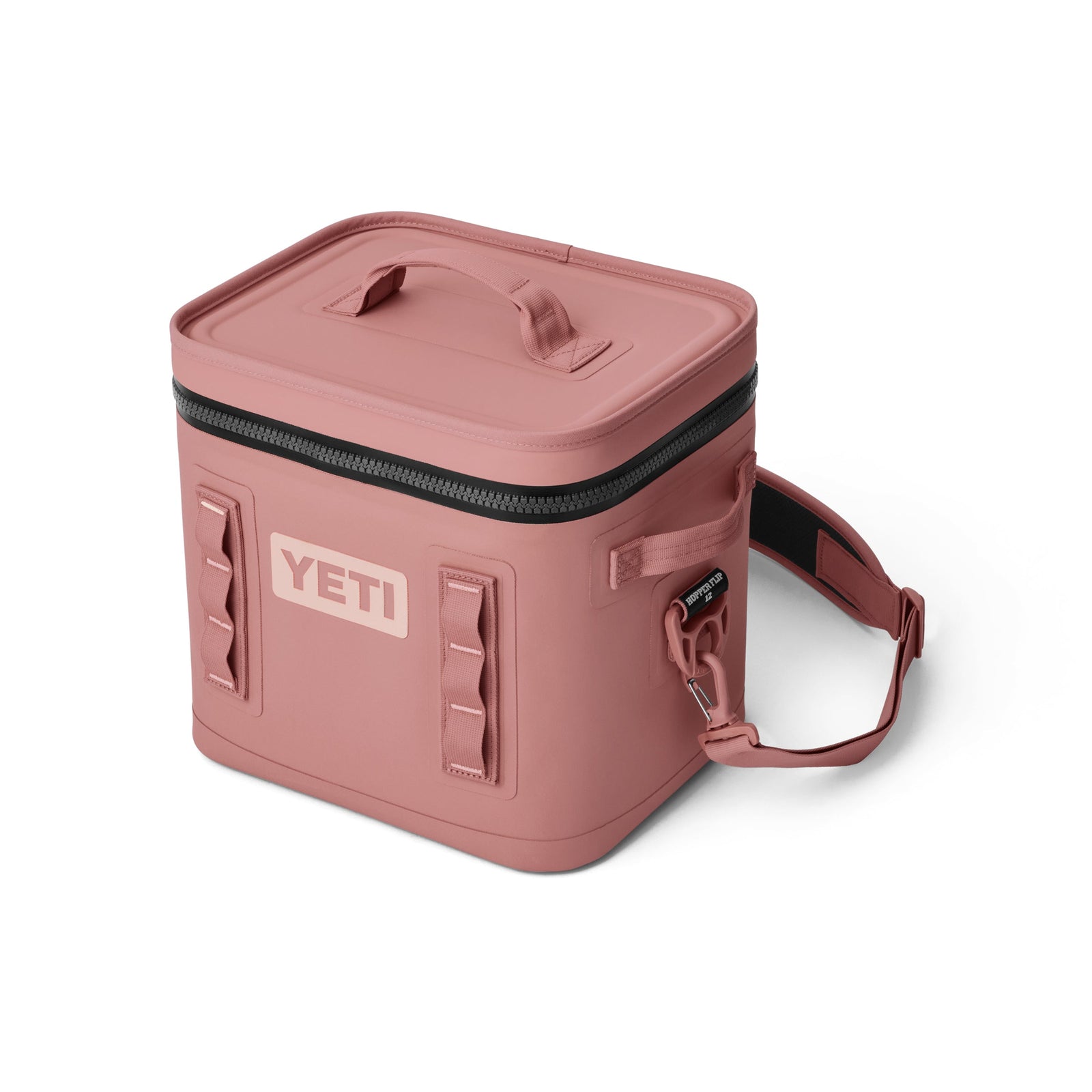 Die YETI® Kühltasche Hopper Flip® 12 in Sandstone Pink verfügt über einen Deckel mit Reißverschluss, einen stabilen Griff, einen verstellbaren Schultergurt und seitliche Schlaufen; die Vorderseite zeigt das YETI-Logo auf dieser stilvollen Kühlbox.