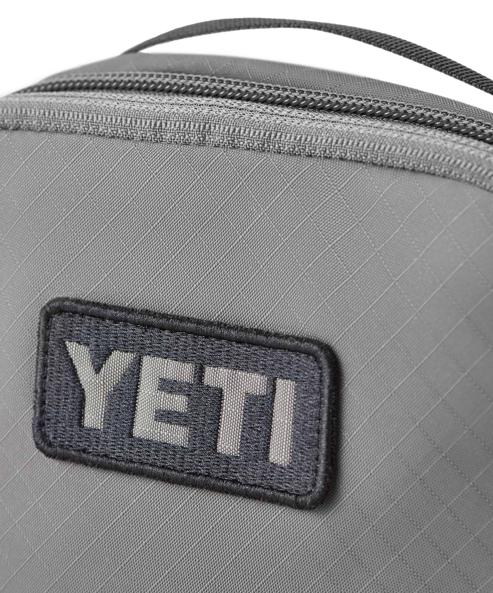 Nahaufnahme einer grauen YETI® Packtaschen - Crossroads Cubes M mit einem schwarz-weißen YETI-Logoaufnäher und einem erweiterbaren Reißverschluss entlang der Oberkante.