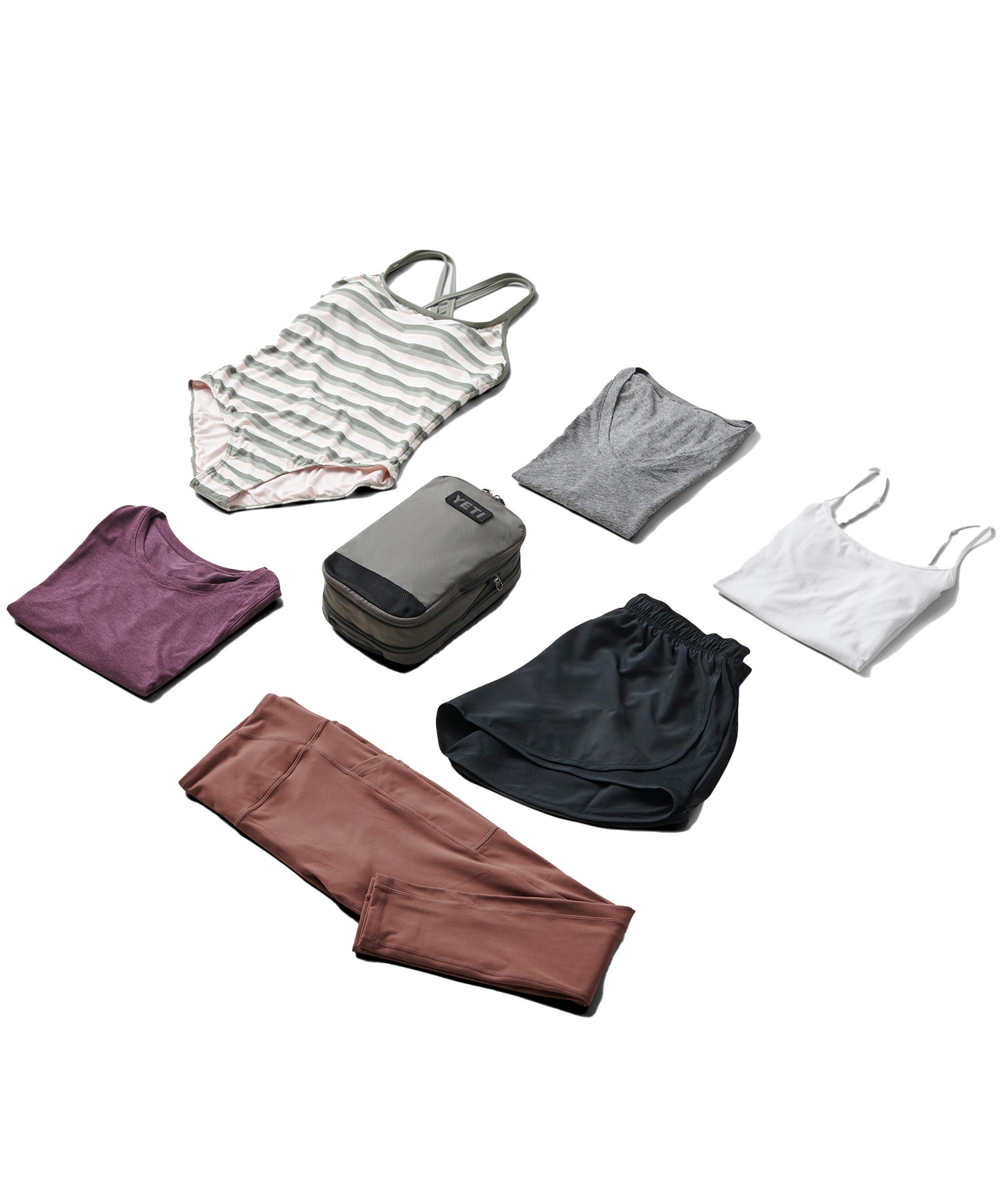 Eine flache Zusammenstellung von Reiseutensilien: gestreifter Badeanzug, lilafarbenes T-Shirt, schwarze Shorts, lilafarbene Leggings und die YETI® Packtaschen - Crossroads Cubes M in Grey-ideal als vielseitige Reise-Packtasche.