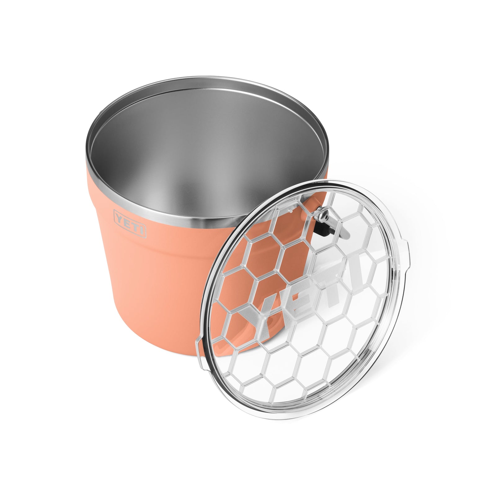 Der YETI® Rambler® 7,6-Liter-Getränkekübel in Lowcountry Peach verfügt über einen Innenraum aus Edelstahl und eine doppelwandige Vakuum-Isolierung. Er wird mit seinem sechseckigen, durchsichtigen Deckel neben dieser stilvollen YETI-Kühlbox gezeigt.