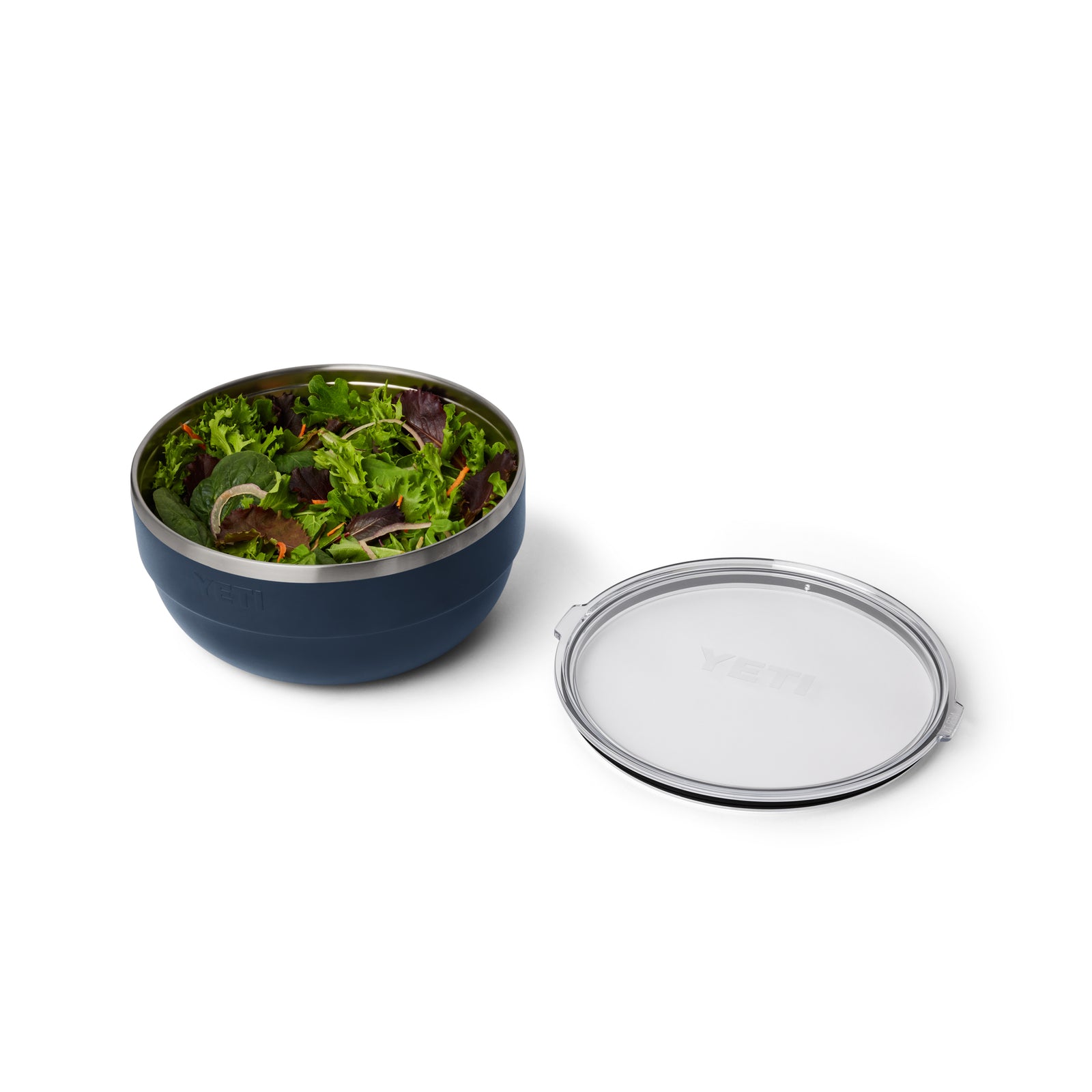 Eine navyfarbene YETI® Rambler Bowl Large von YETI, gefüllt mit grünem Blattsalat, steht neben einem durchsichtigen runden Kunststoffdeckel auf weißem Hintergrund.